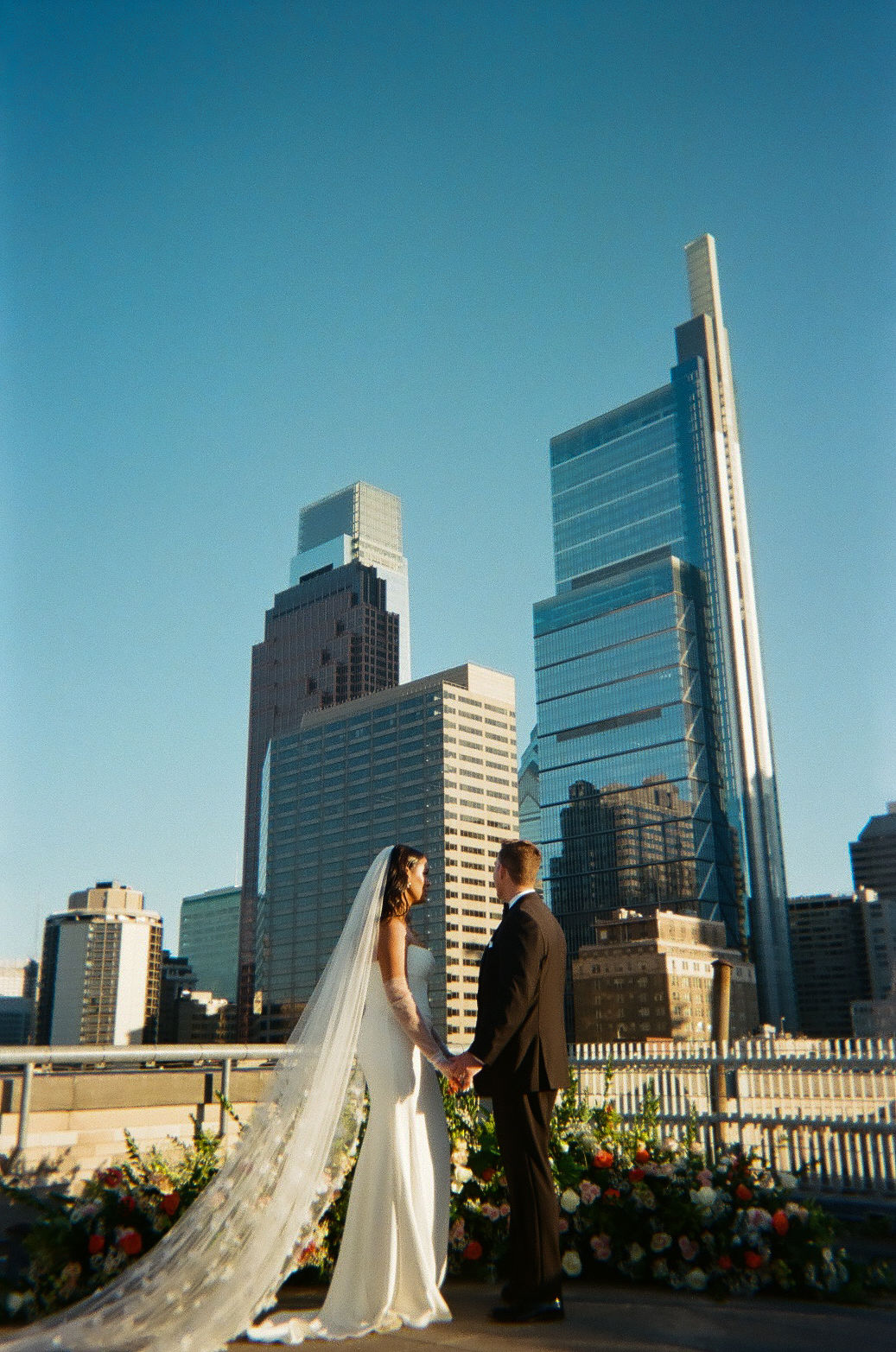 bride and groom holding hands on the roof of the Franklin Institute and looking off at the skyscrapers in the distance