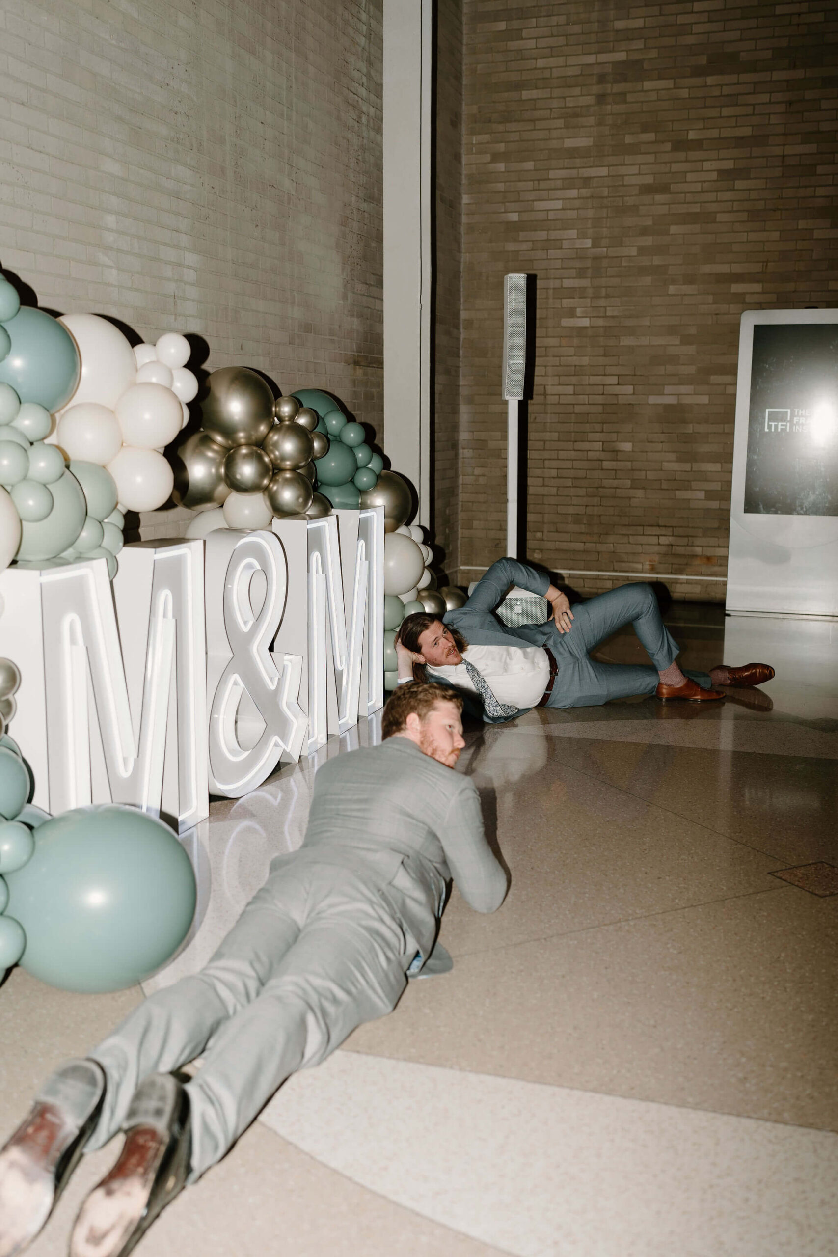 two men laying on the ground and posing in front of the M&M sign