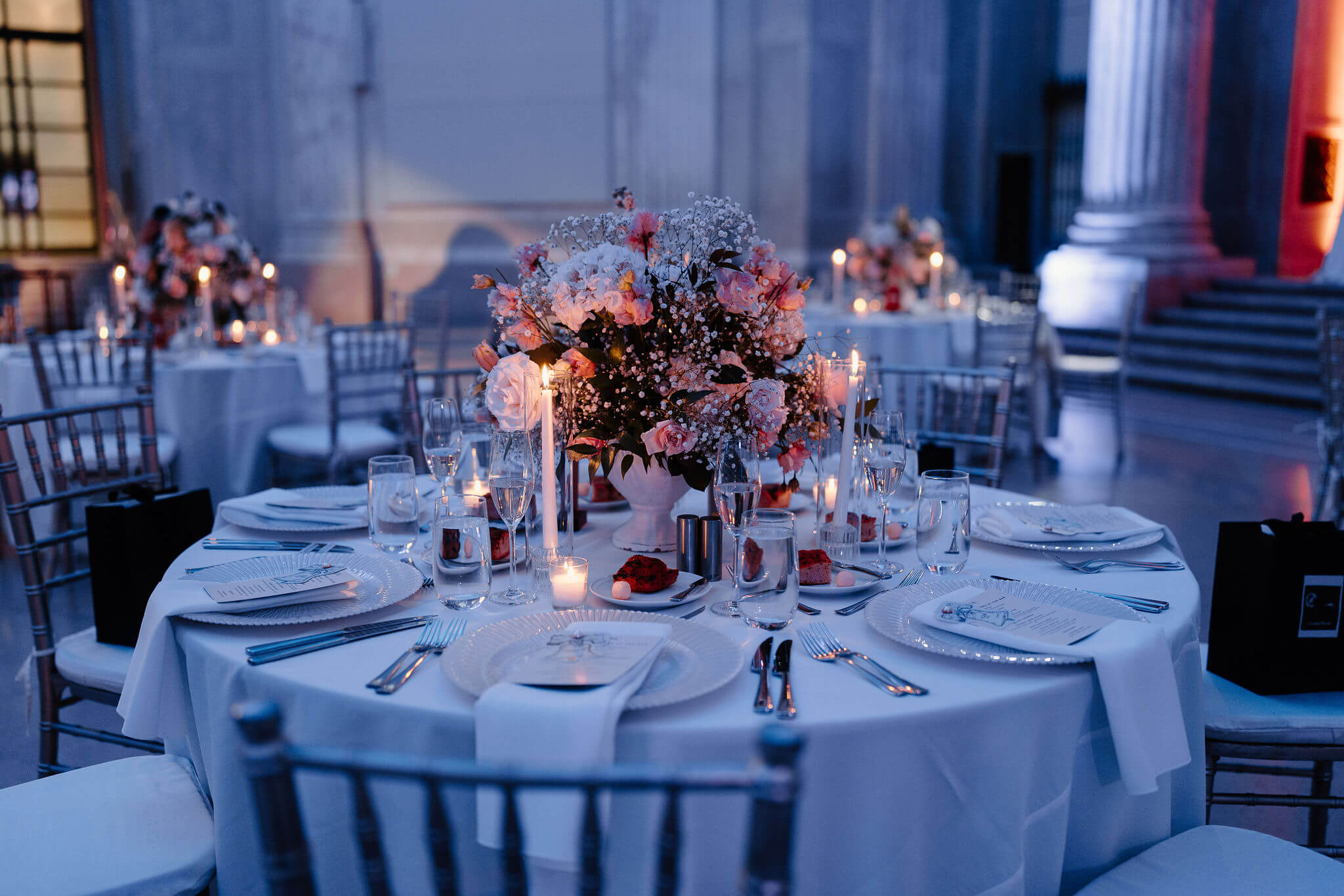 a purple-hued image of a wedding reception centerpiece, featuring a large floral bouquet and tall candlesticks at the Franklin Institute