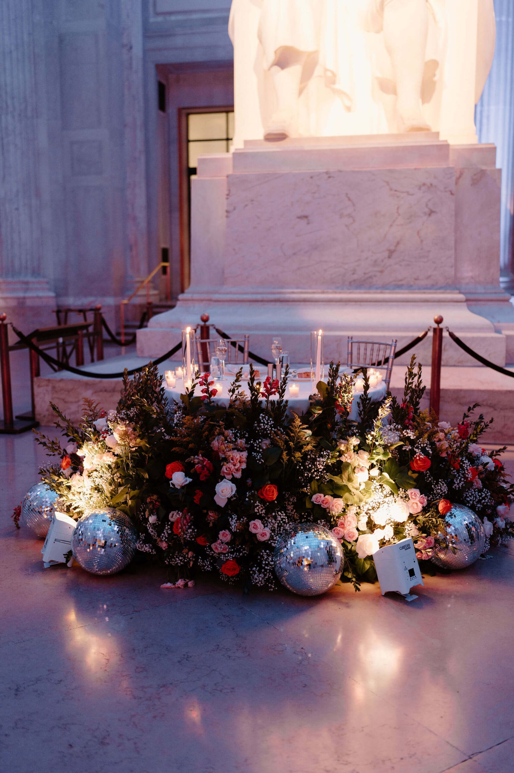 a pink-and-purple hued image of the sweetheart table at the wedding reception, with a large floral installation and disco balls