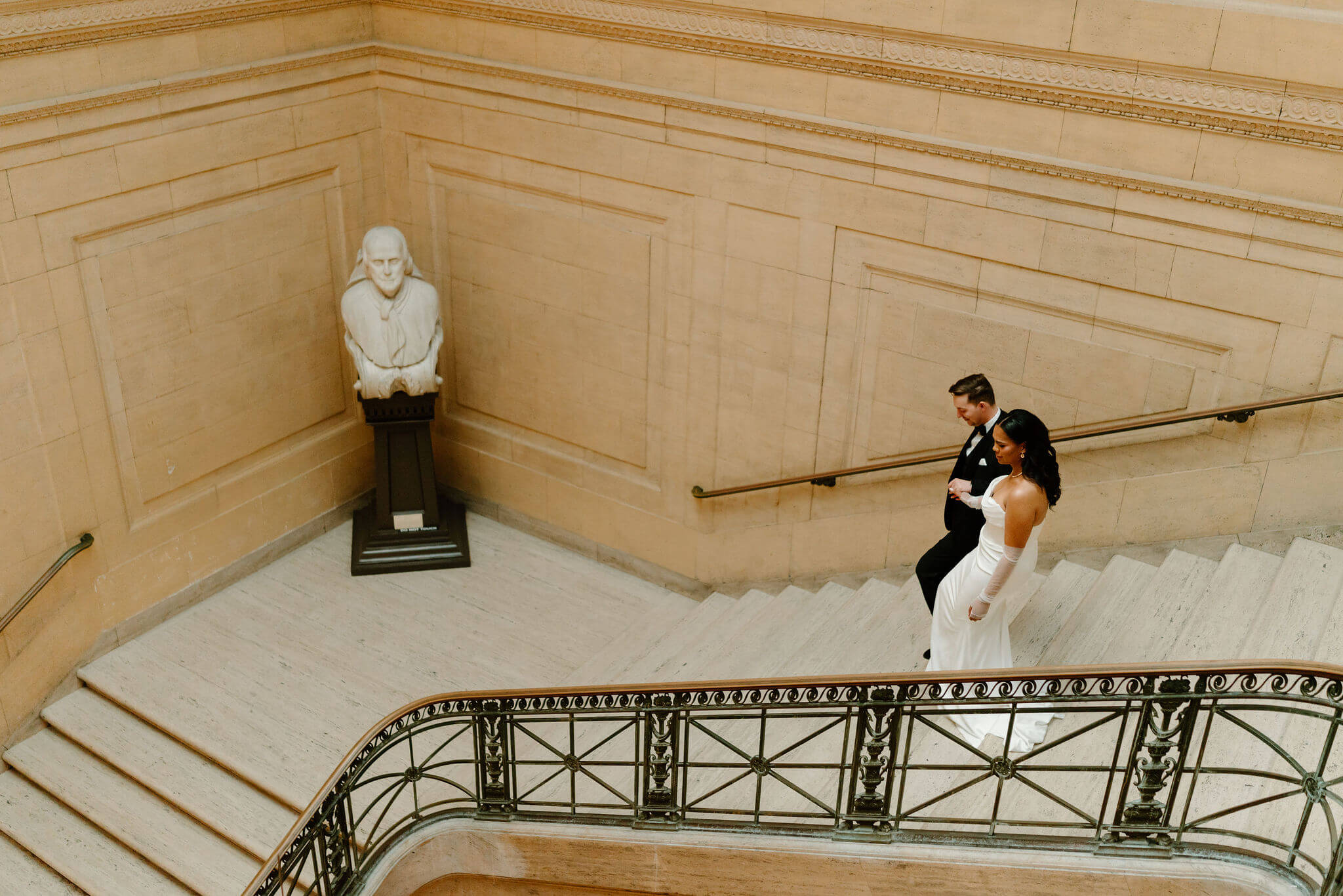 aerial image of a groom leading his bride down a large marble staircase at their franklin institute wedding