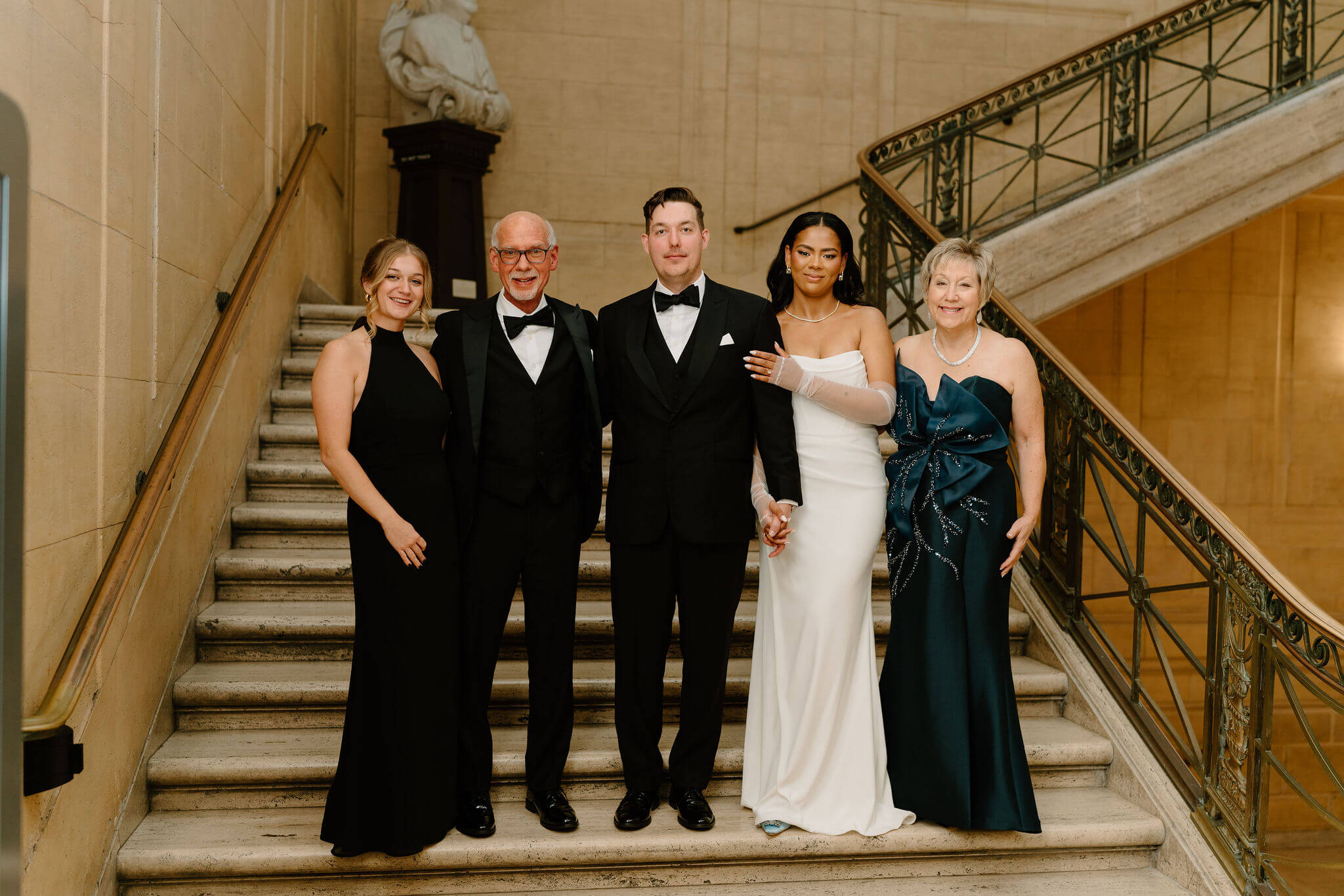 bride and groom smiling with his parents and sister, all on a marble staircase in formalwear