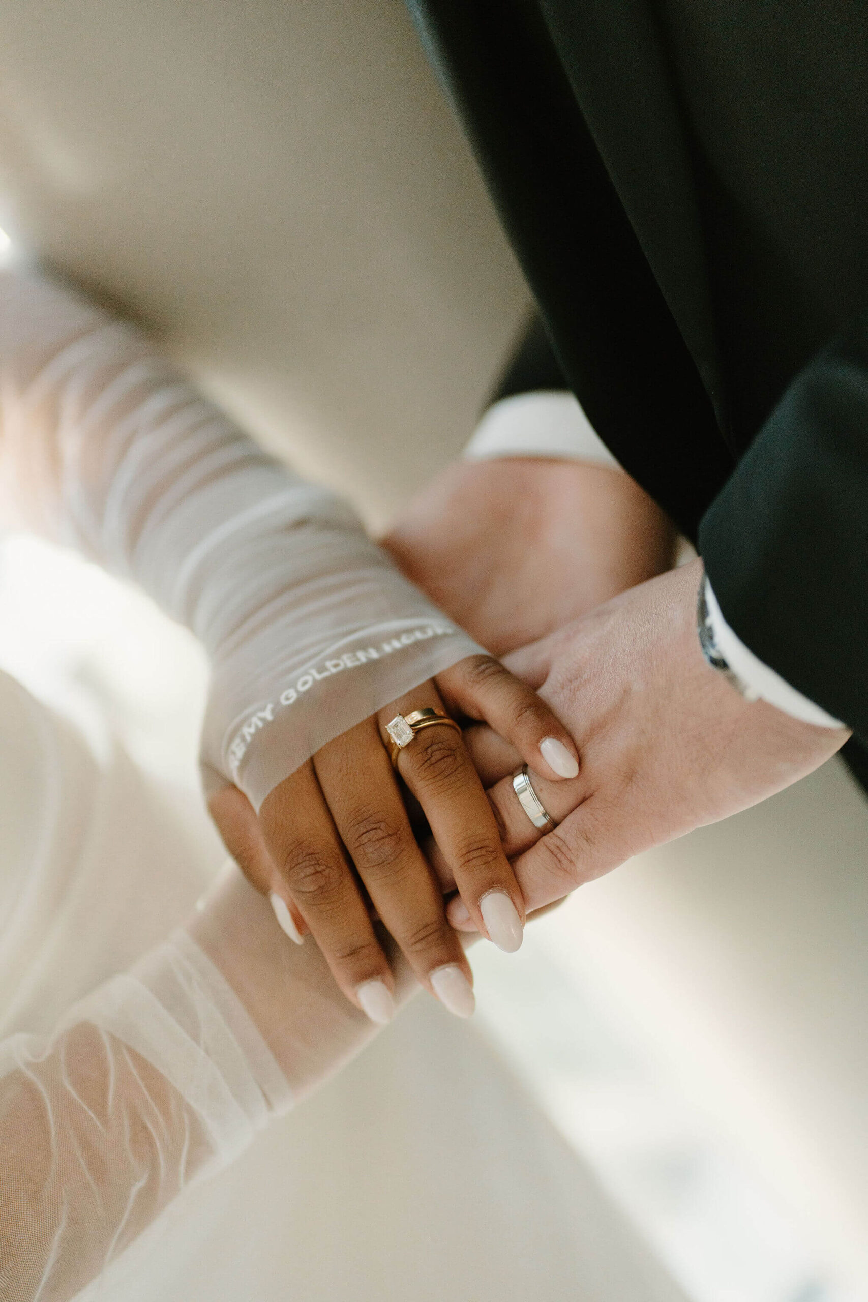 close up of bride and groom's bands, focused on their wedding rings and the bride's sheer fingerless gloves that read "you're my golden hour"
