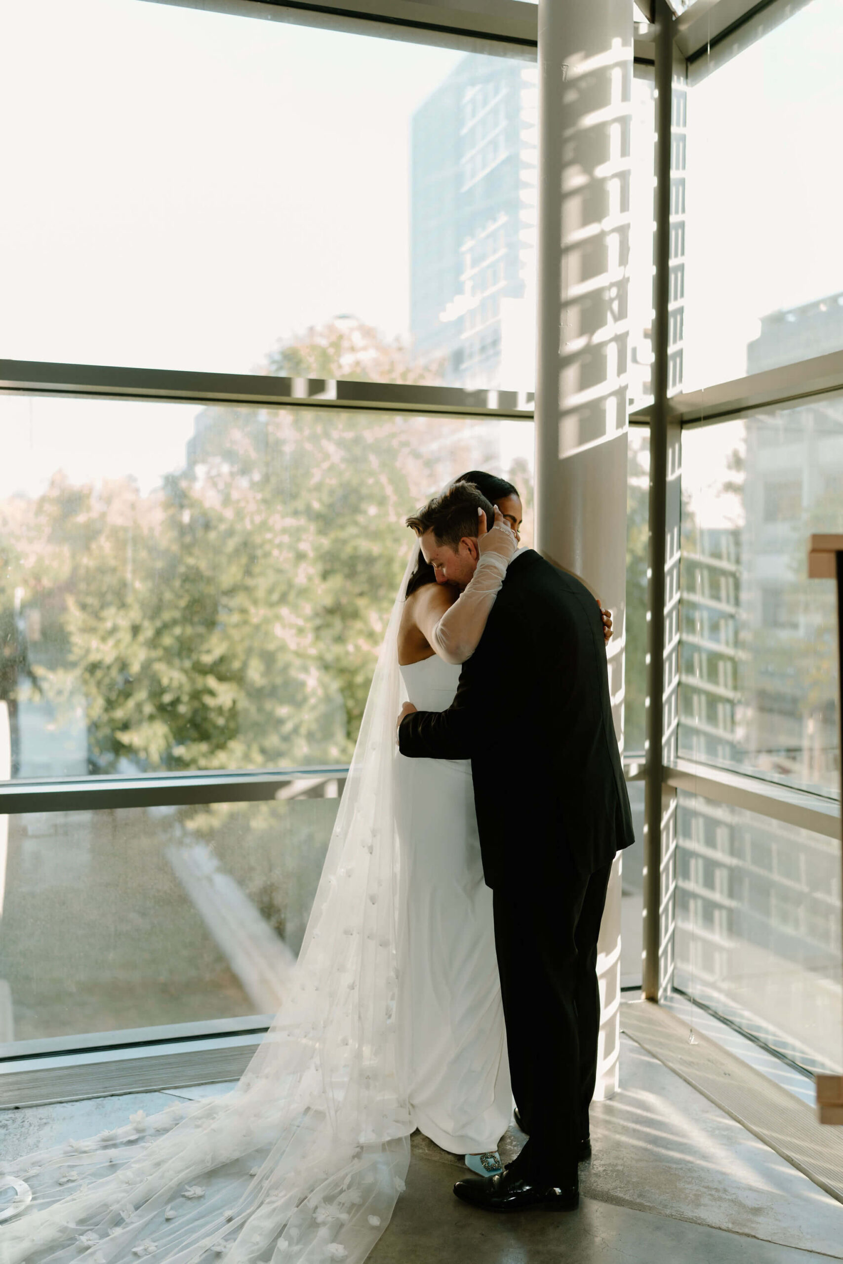 bride and groom hugging tightly in front of a large window