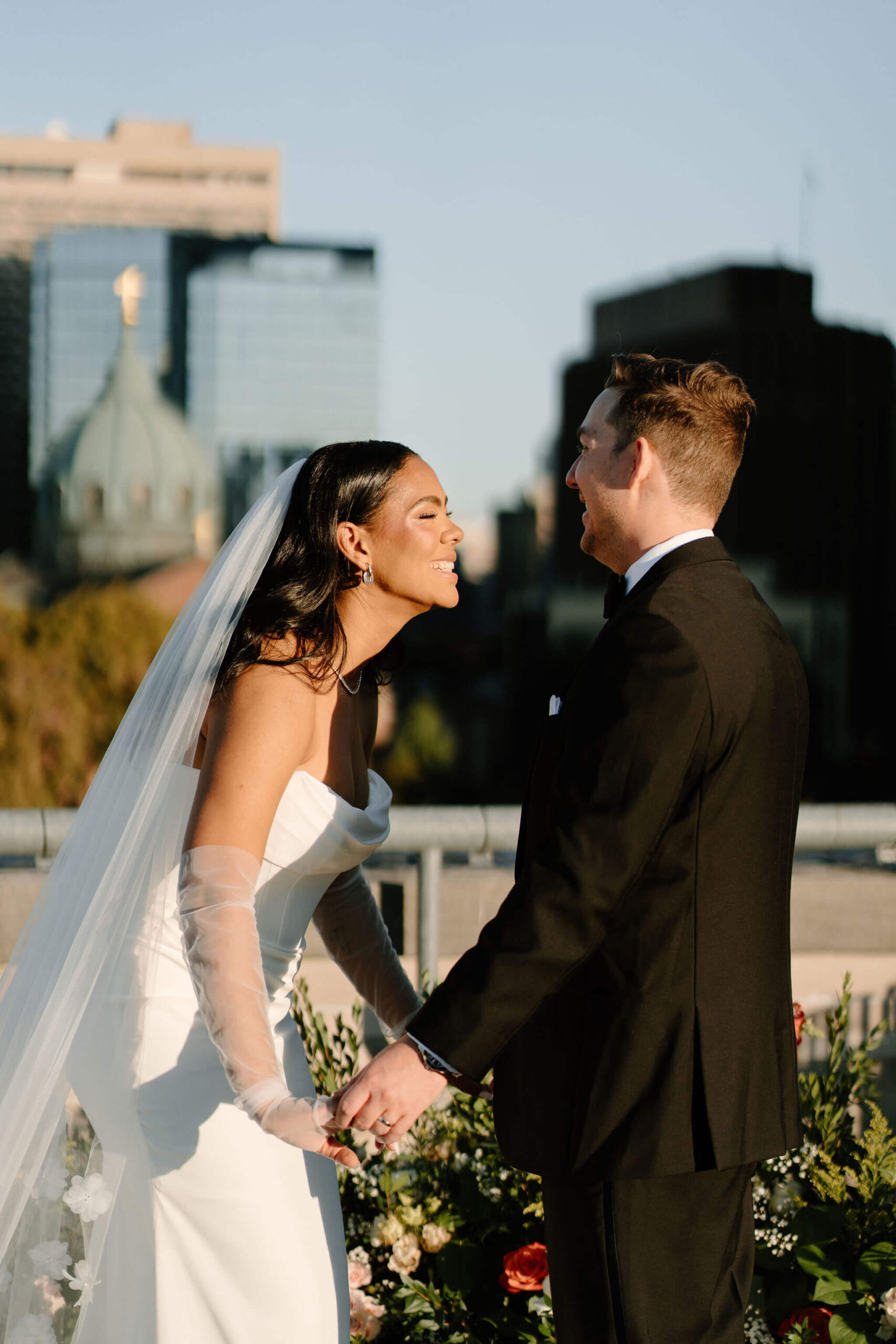close up of bride and groom holding hands on the roof of the Franklin Institute and laughing toward each other