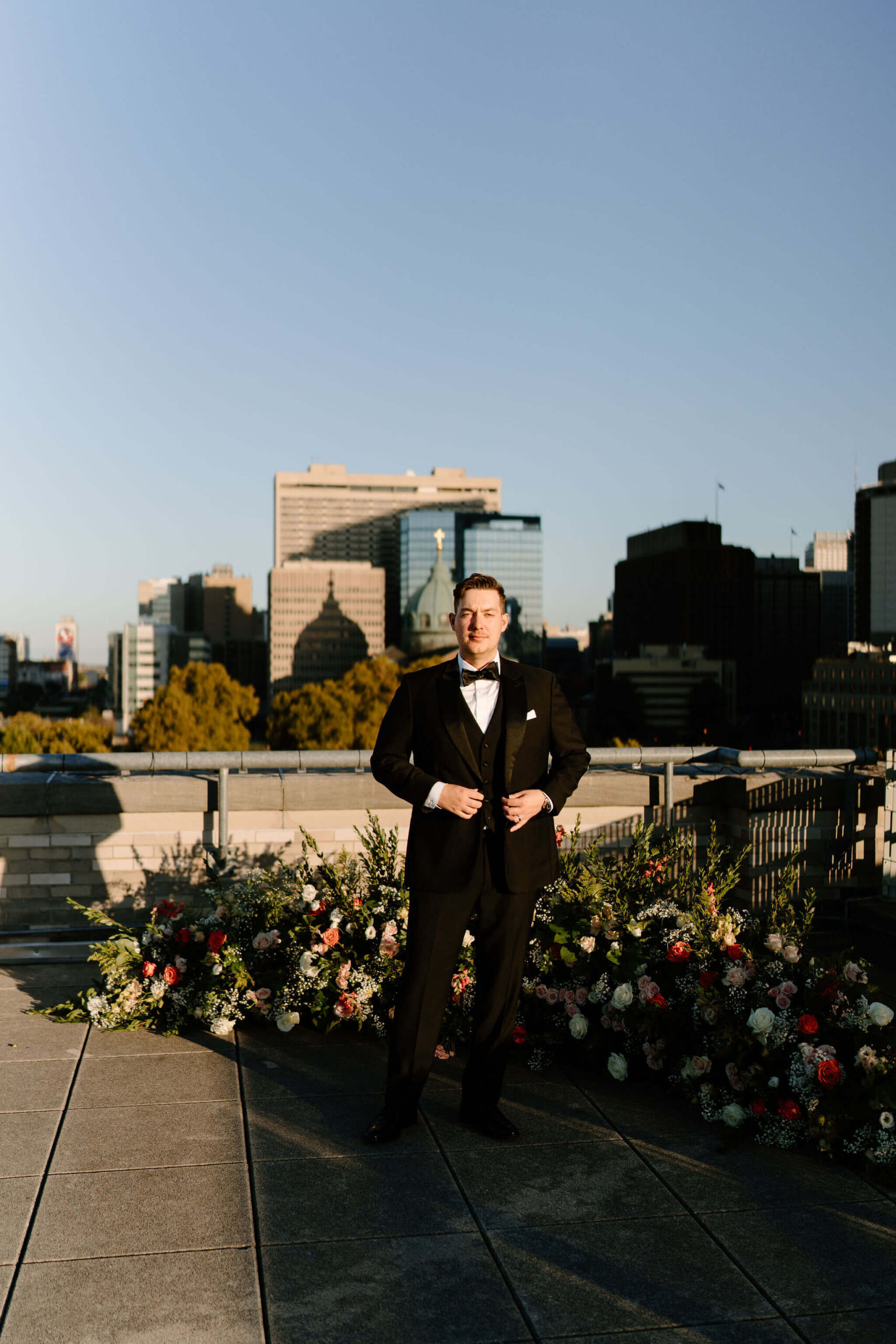 groom standing in direct sun on the roof of the Franklin Institute, staring into the camera with the Philadelphia skyline in the distance