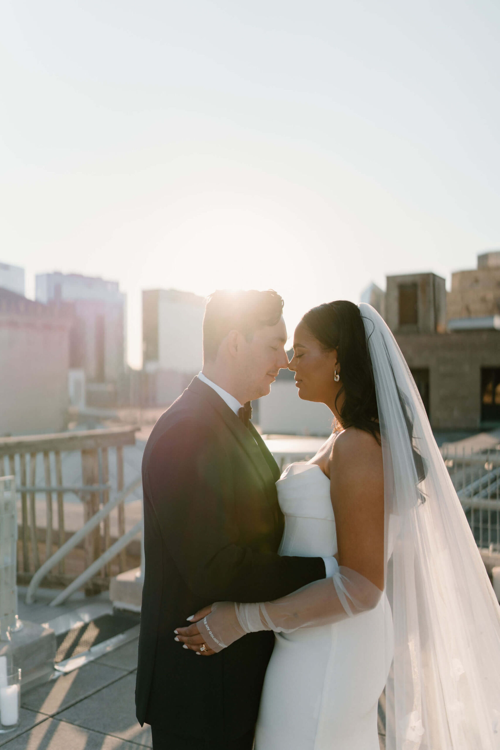 bride and groom, backlit by the sun, embracing with eyes closed
