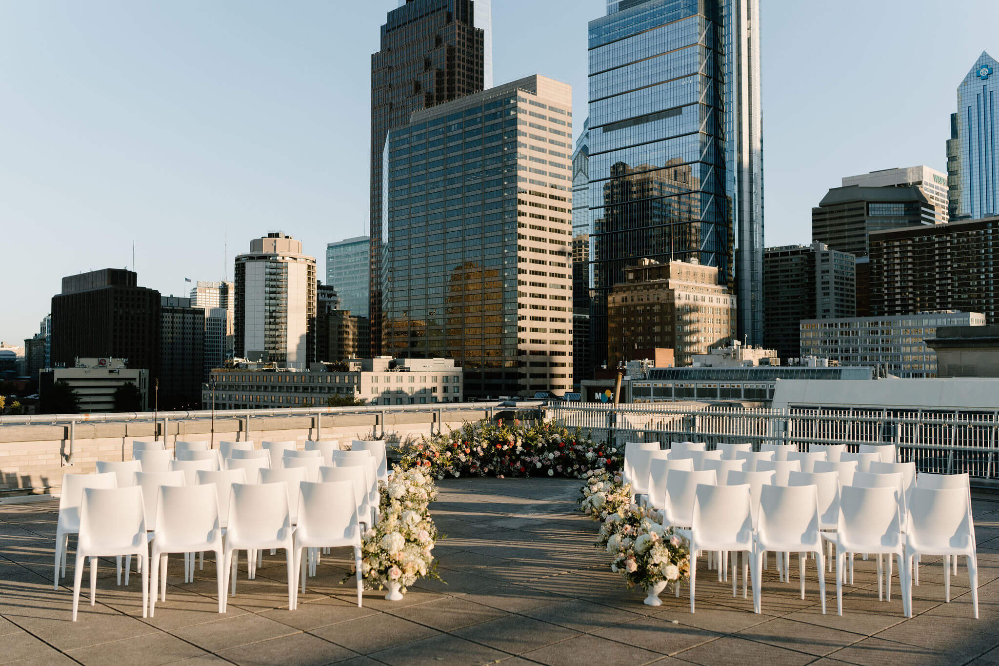 wedding ceremony set up on the roof of the Franklin Institute, facing the Philadelphia Skyline, with white chairs and colorful flowers running down the aisle