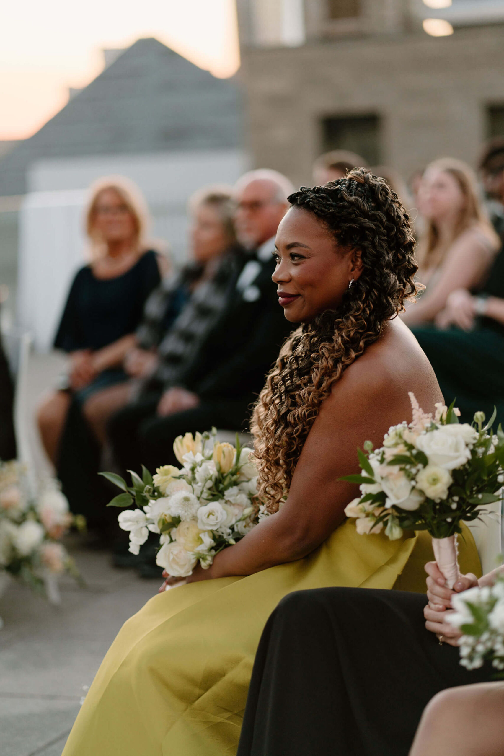 mother of the bride seated, holding bride's bouquet, smiling during the wedding ceremony