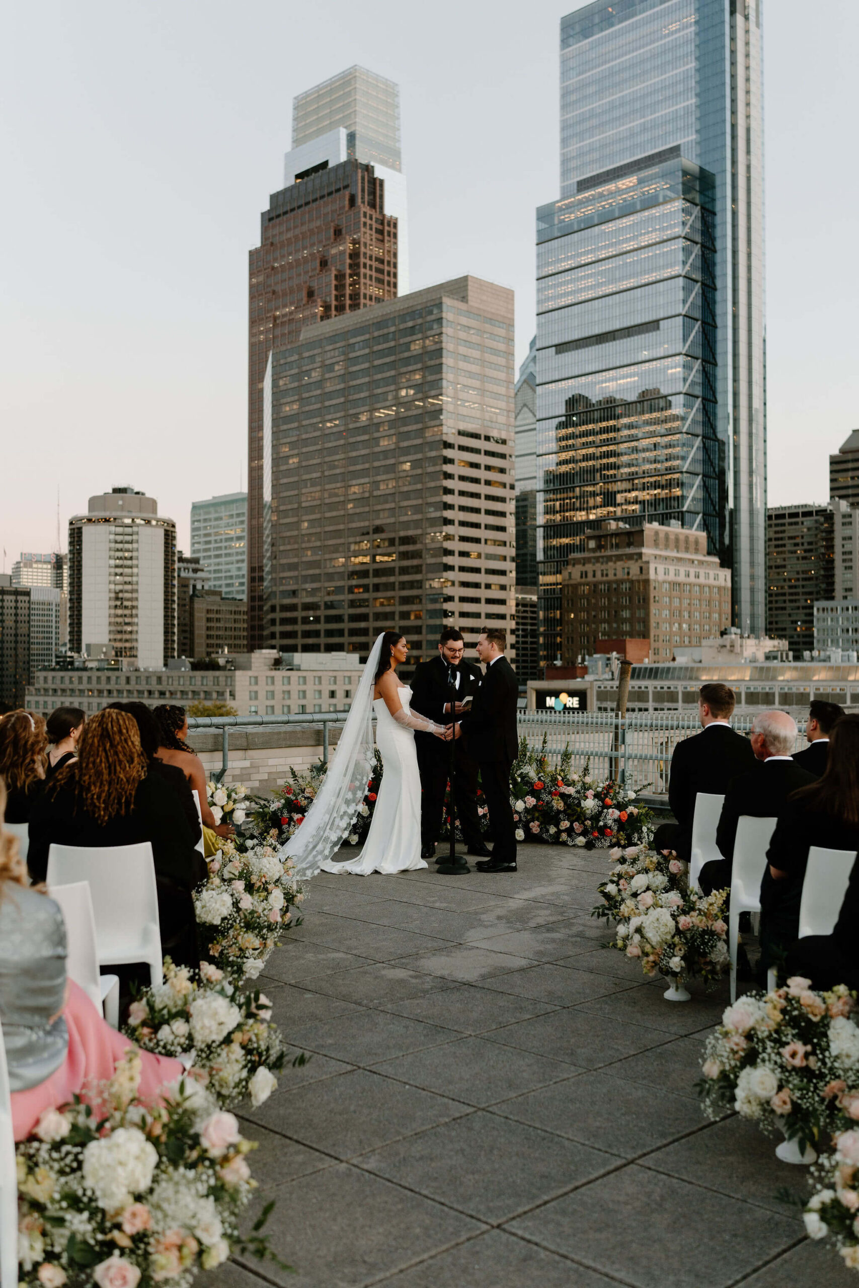 bride and groom holding hands during their wedding ceremony at sunset on the roof of the Franklin Institute, the city skyline behind them