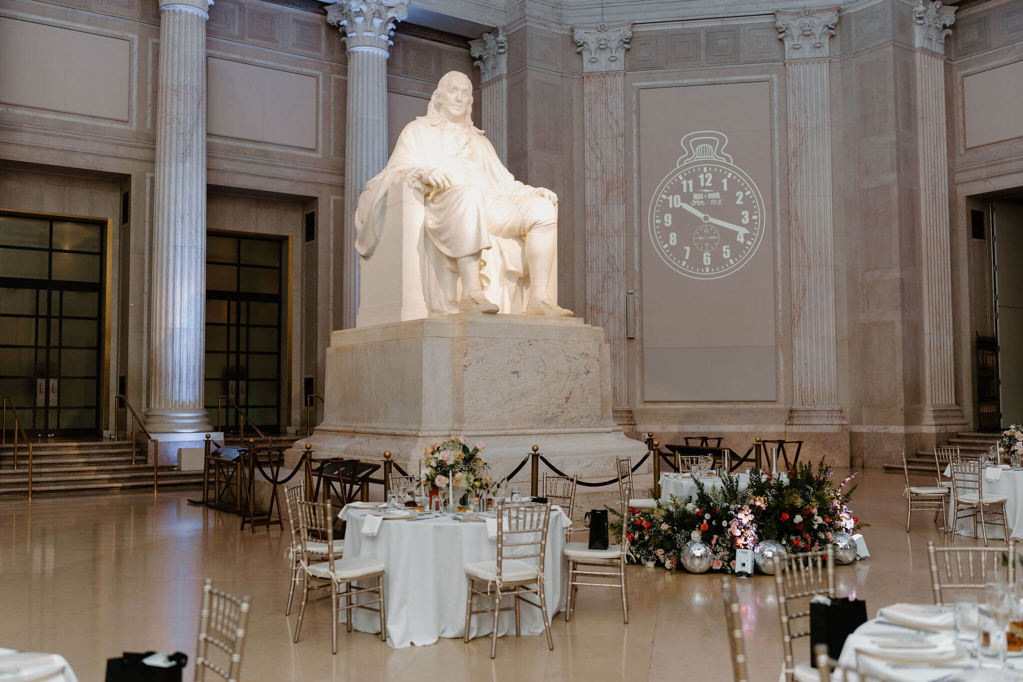 interior image of the ballroom at the Franklin Institute, featuring the enormous statue of Ben Franklin, surrounded by white-linen tables of a wedding reception