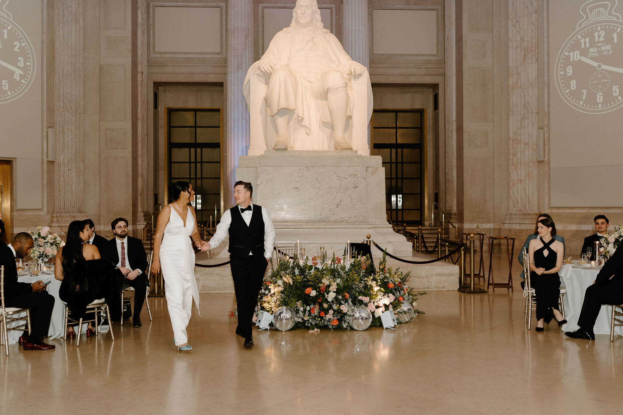 bride and groom walking onto the dance floor during their wedding reception in Benjamin Franklin Hall, an enormous statue of Benjamin Franklin behind them