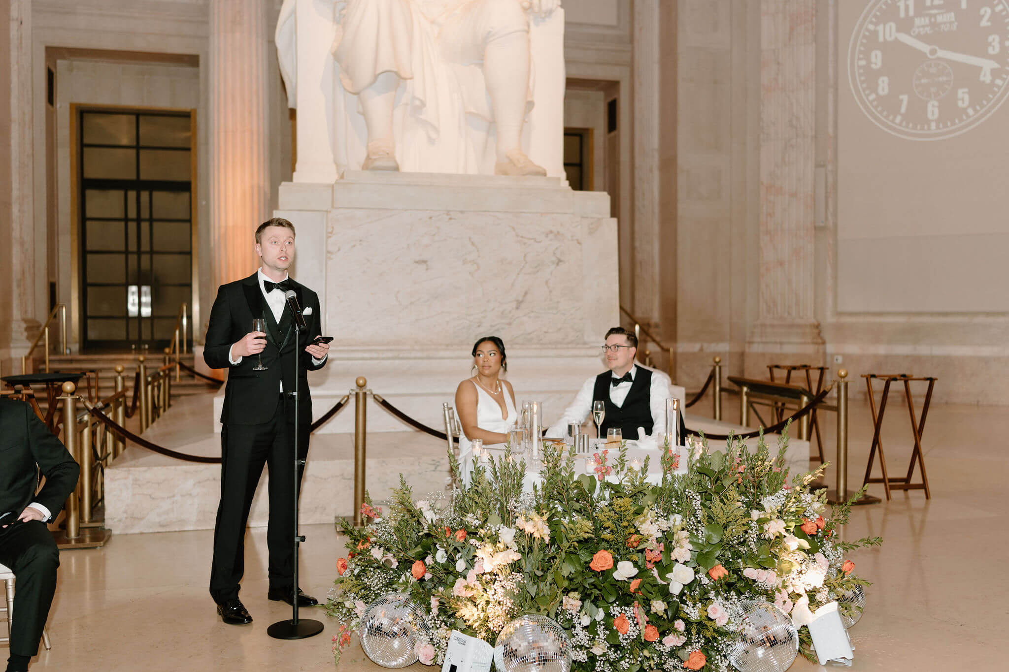 one best man giving a speech during a wedding reception, standing next to the sweetheart table