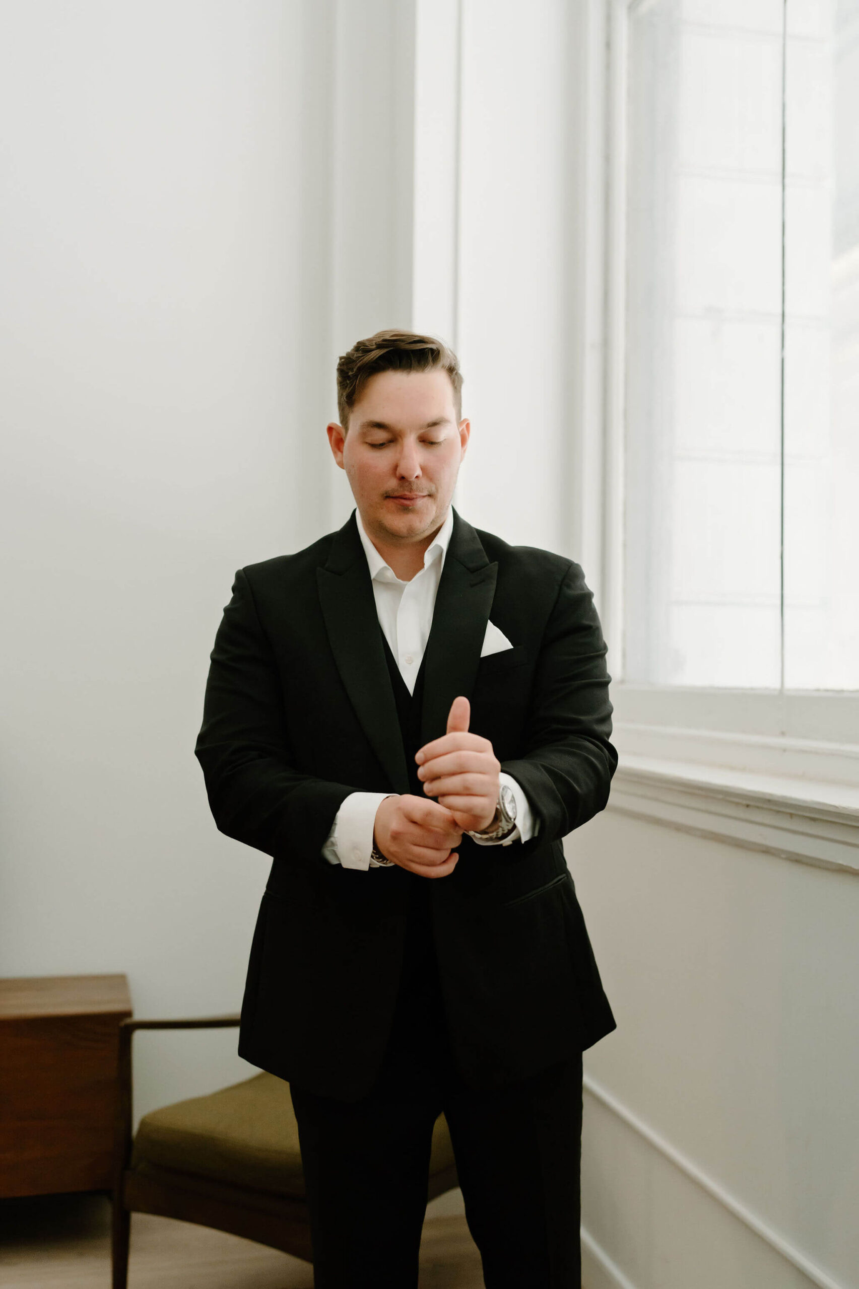 groom in black suit fixing his cuff links