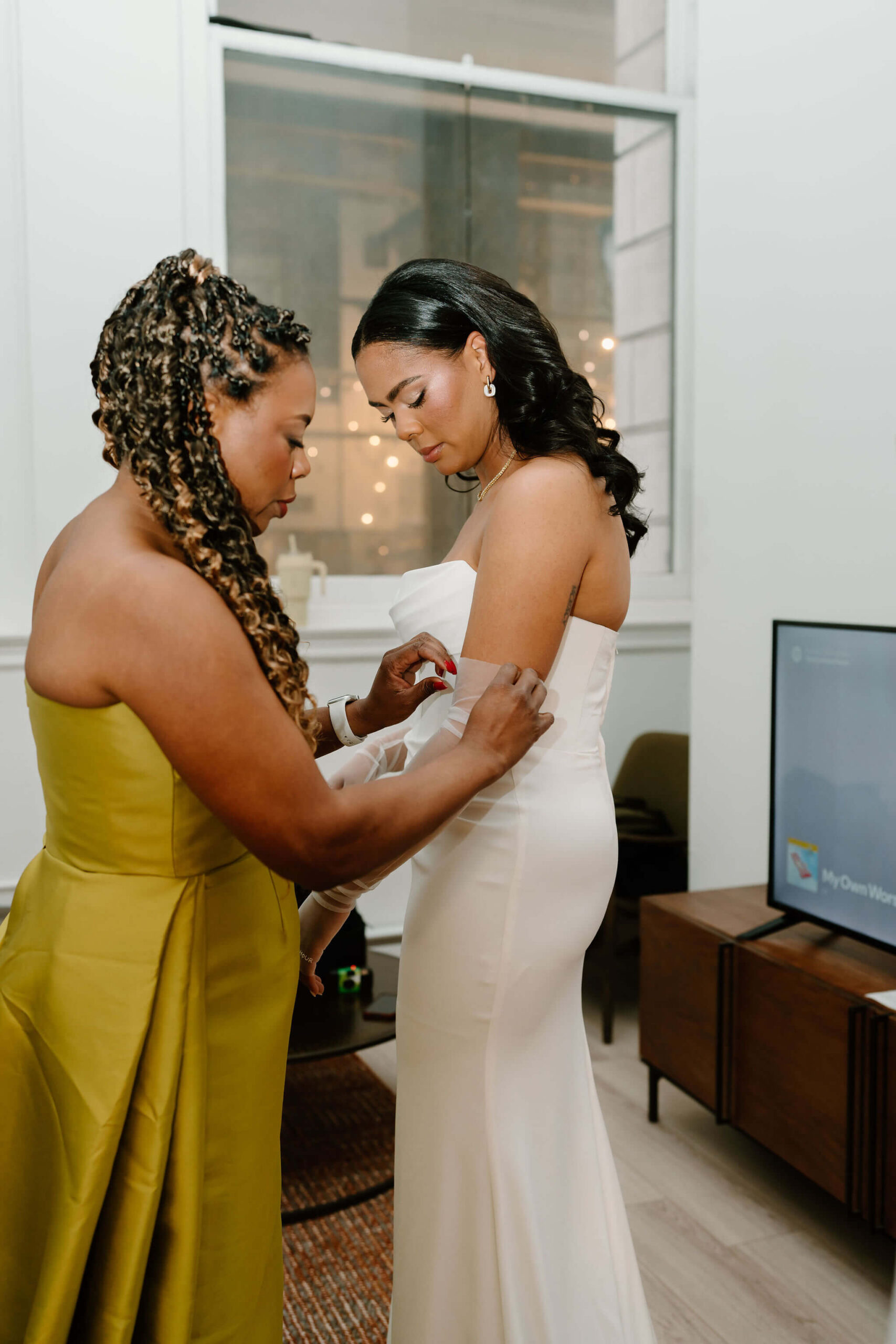mother of the bride helping bride to pull up her sheer gloves