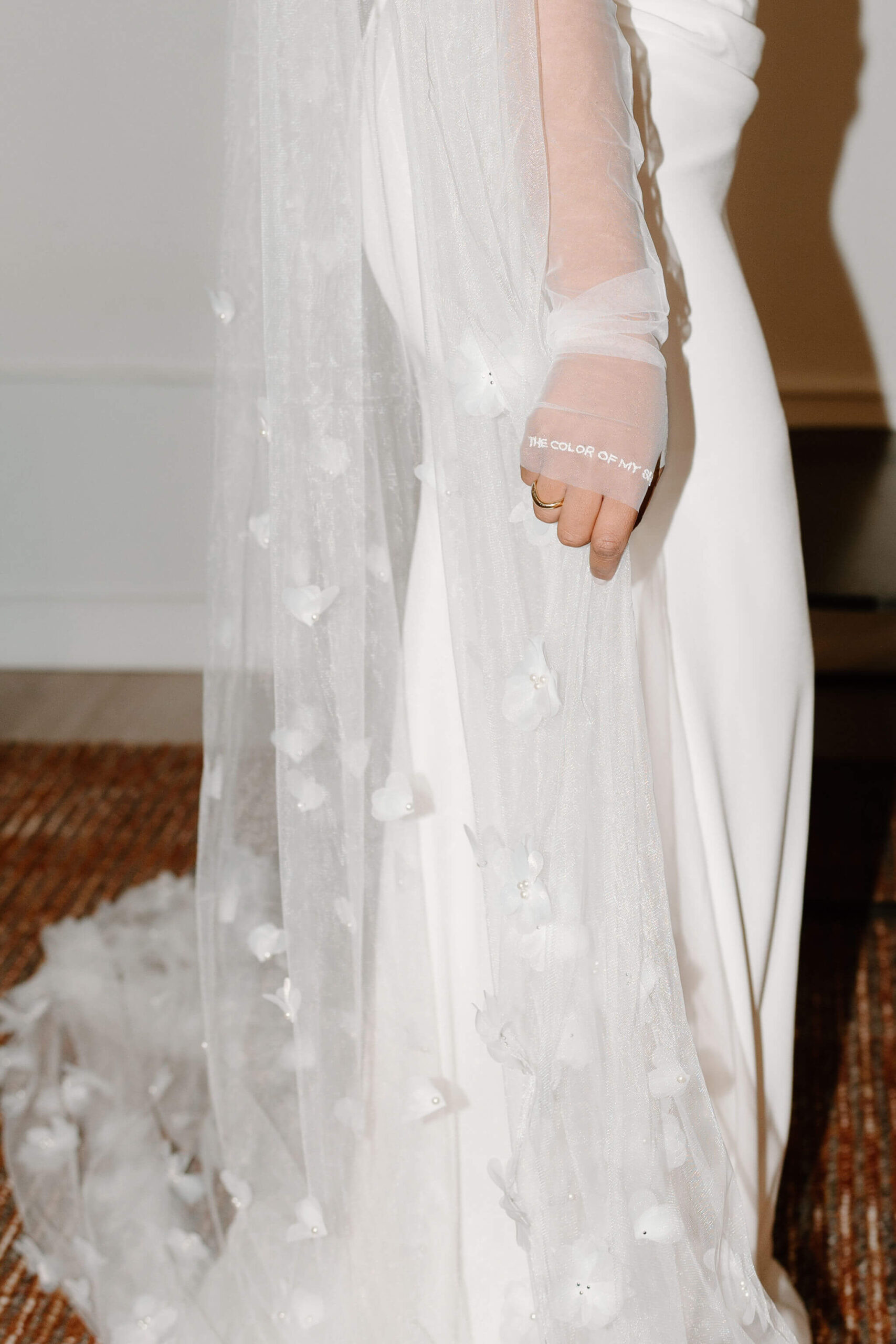 close up of bride's hand holding her veil with a ring on her finger, the words written on her sheer gloves "the color of my sky"