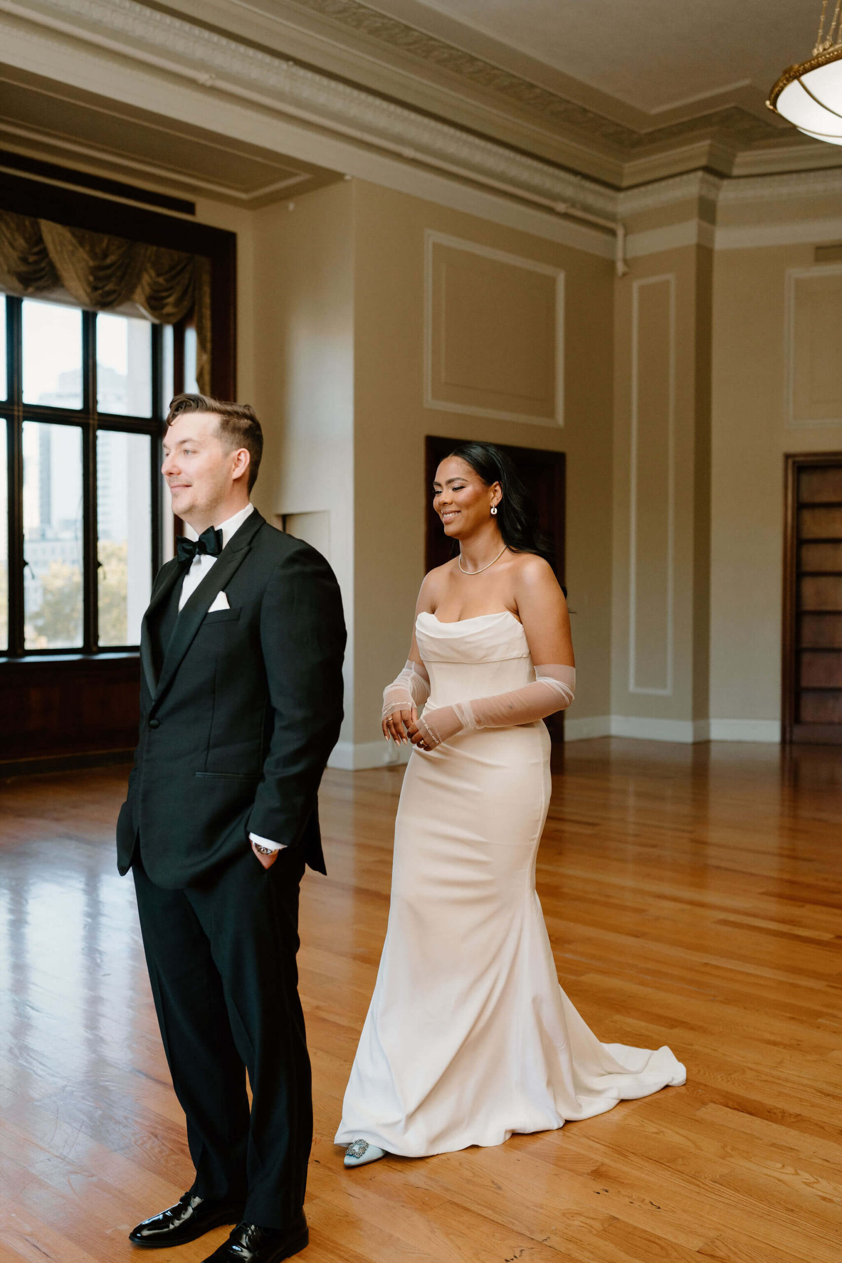 bride in white wedding dress coming up behind groom for their first look, both grinning with excitement