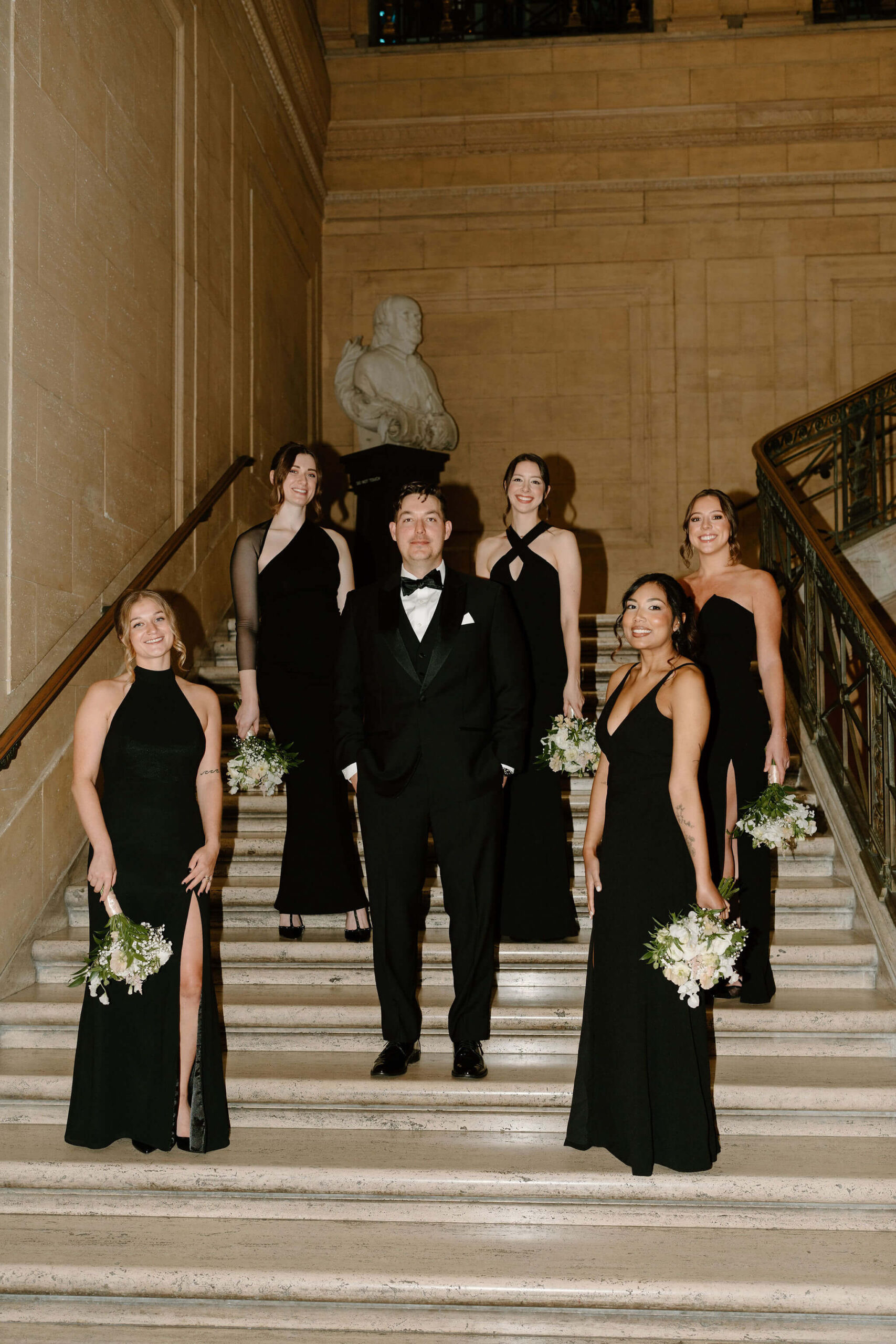 groom and bridesmaids all looking at the camera while standing staggered on a marble staircase