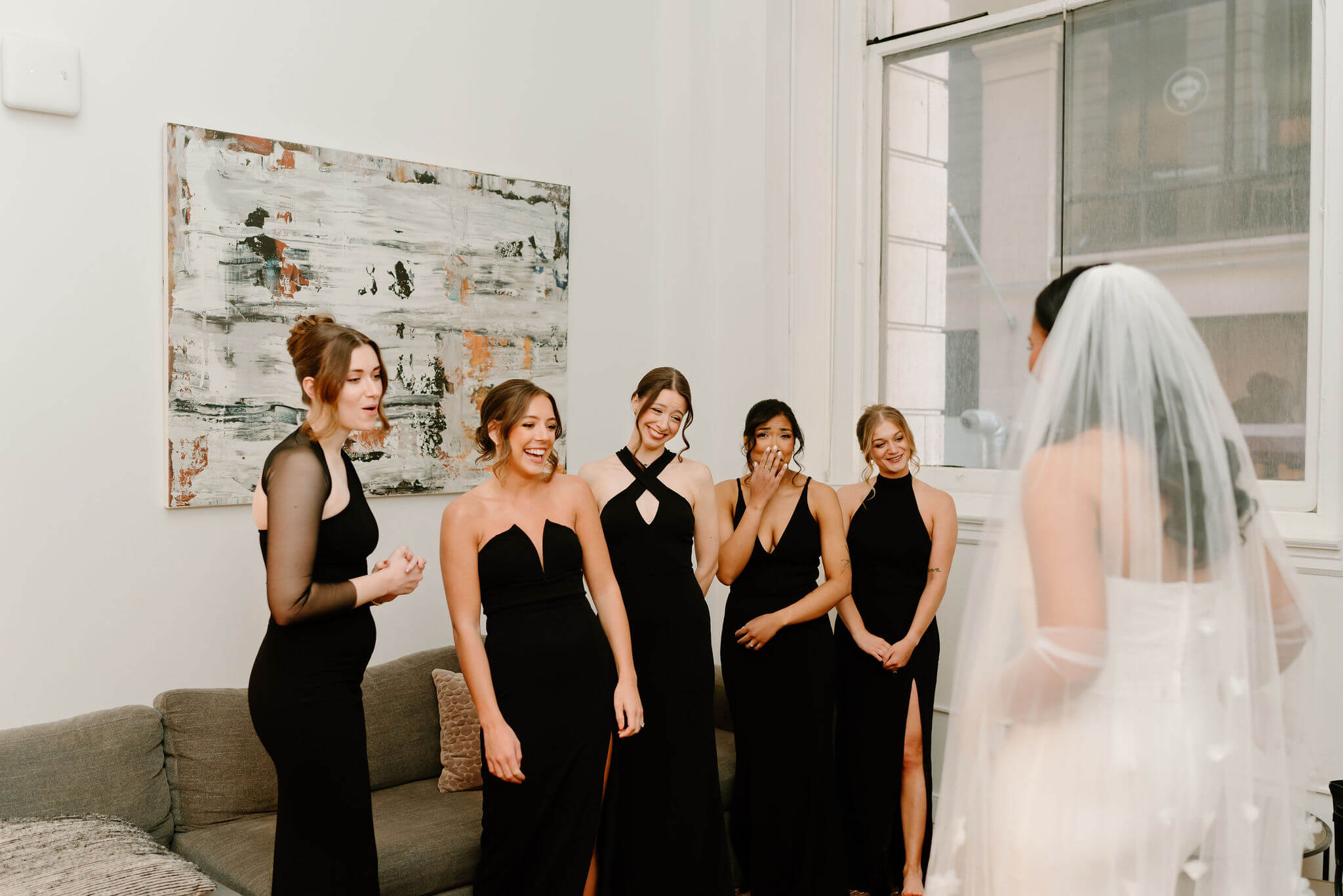 first look of bride with her bridesmaids, smiling widely and wearing mismatched black bridesmaids dresses