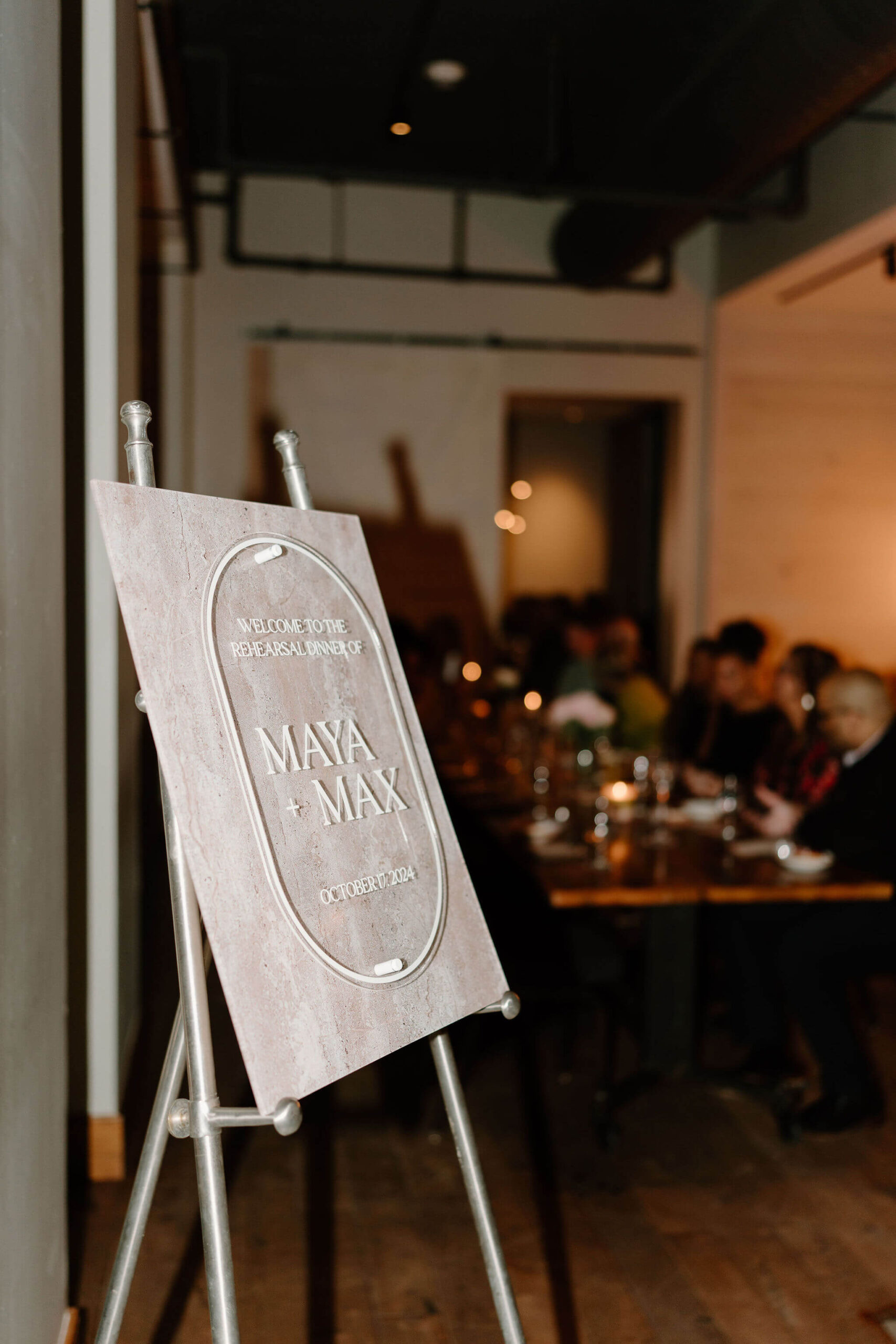 close up of welcome sign to the rehearsal dinner for Maya & Max, with the table of guests enjoying dinner out of focus in the background