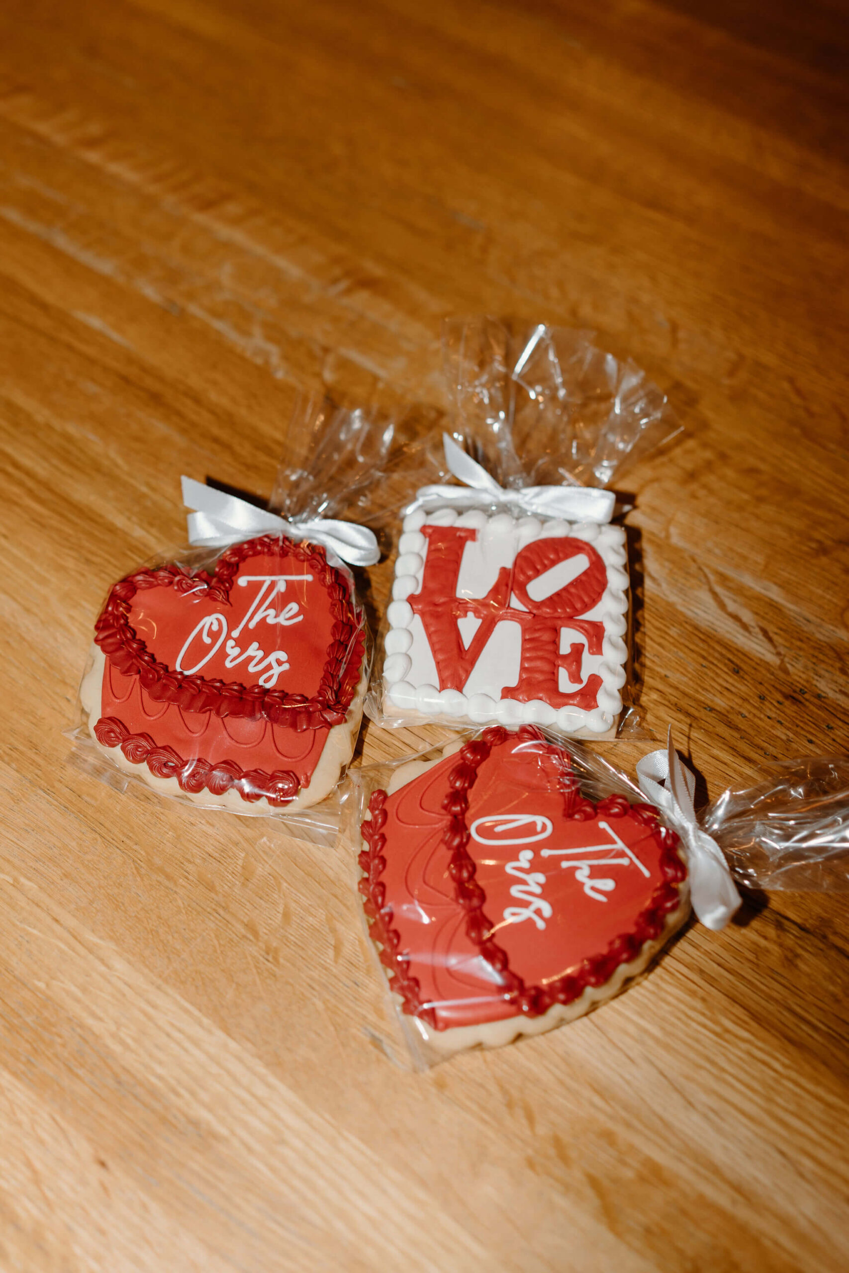close up of custom sugar cookies, one heart-shaped red cookie with white script reading "the Orrs", and one white square-shaped cookie with red letters spelling out "LOVE" in the same style as the sign at Love Park, in Philadelphia