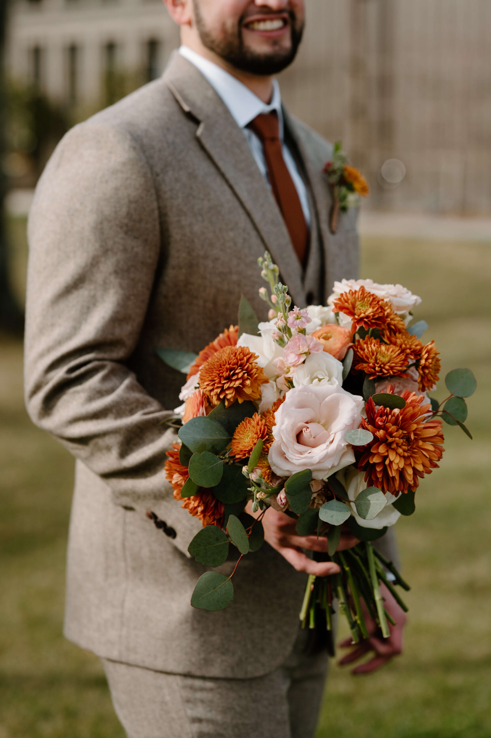 groom smiling widely, holding bride's orange and red bouquet