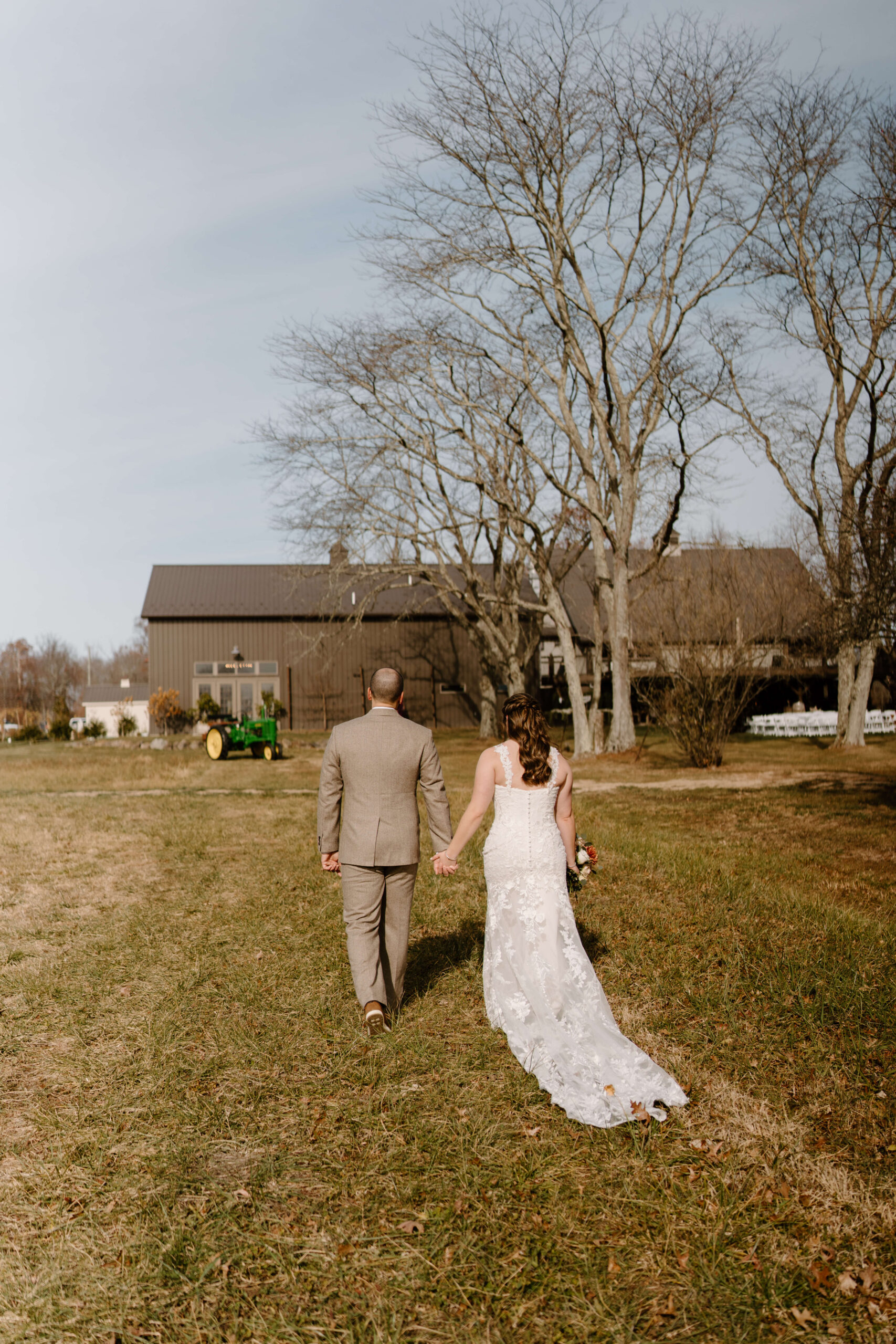 bride and groom walking away from the camera toward a large brown barn, an antique John Deere tractor in the background