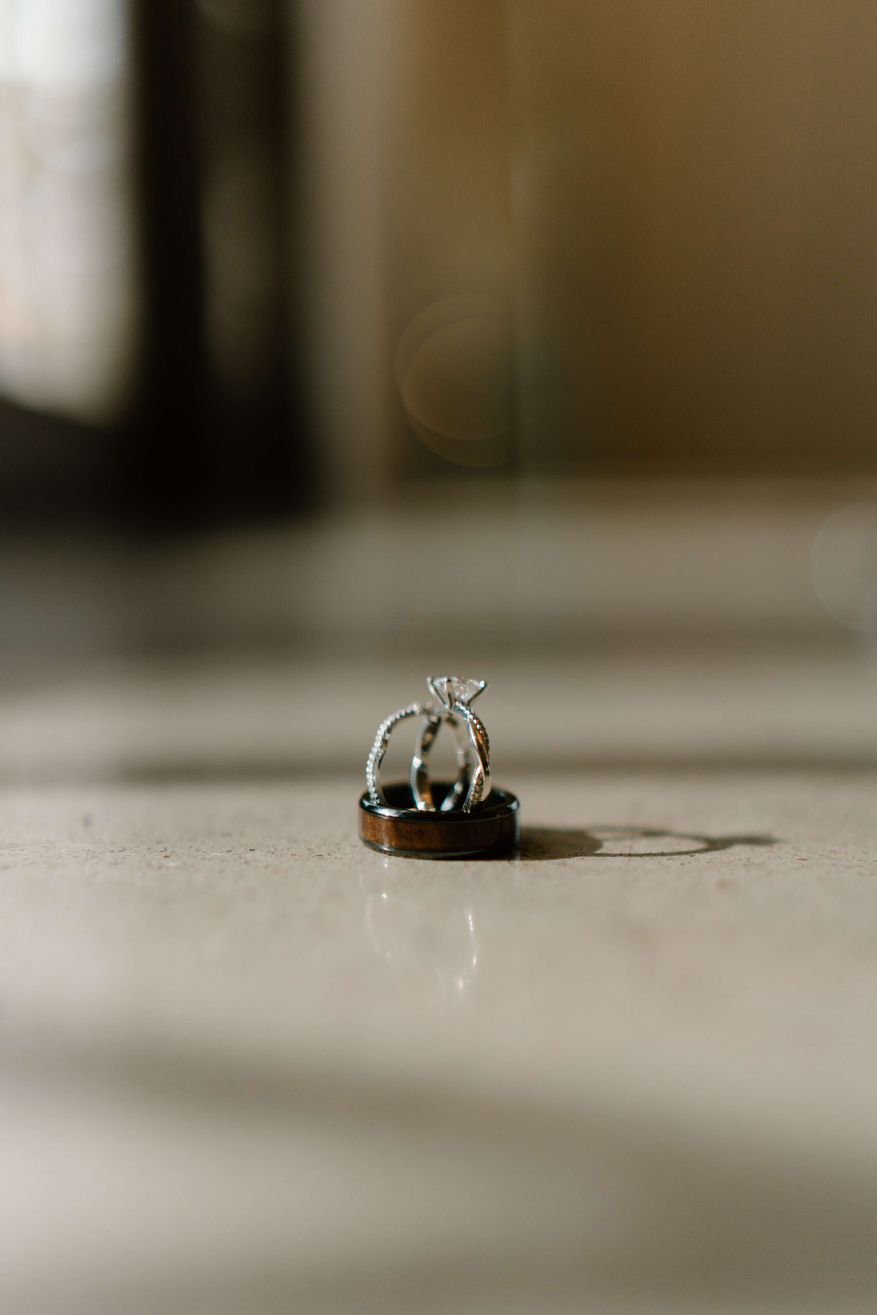 bride's engagement ring and wedding band propped up inside groom's wedding band, casting an interesting shadow on the surface next to it