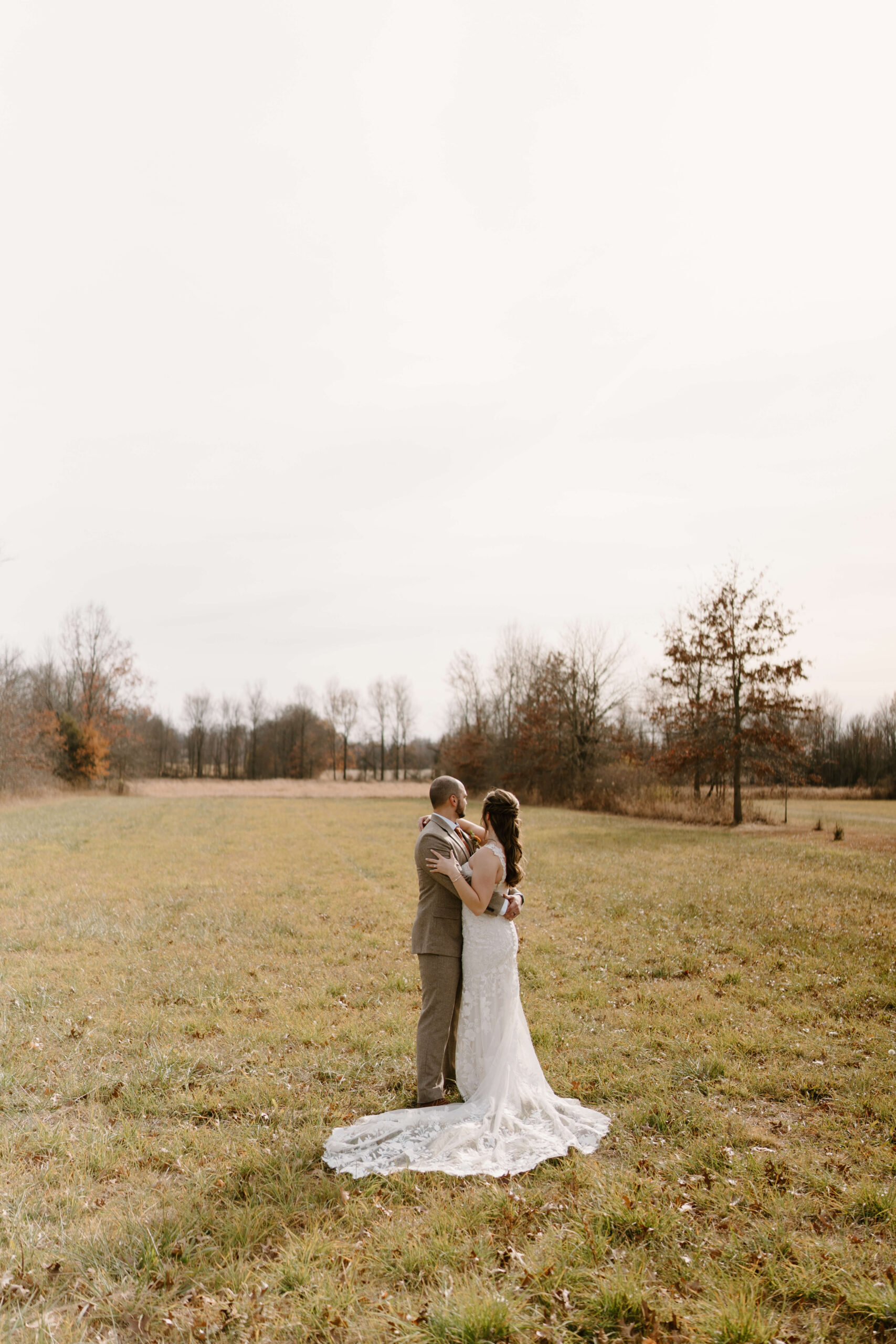 bride and groom embracing in an open field at their November wedding at the Farm