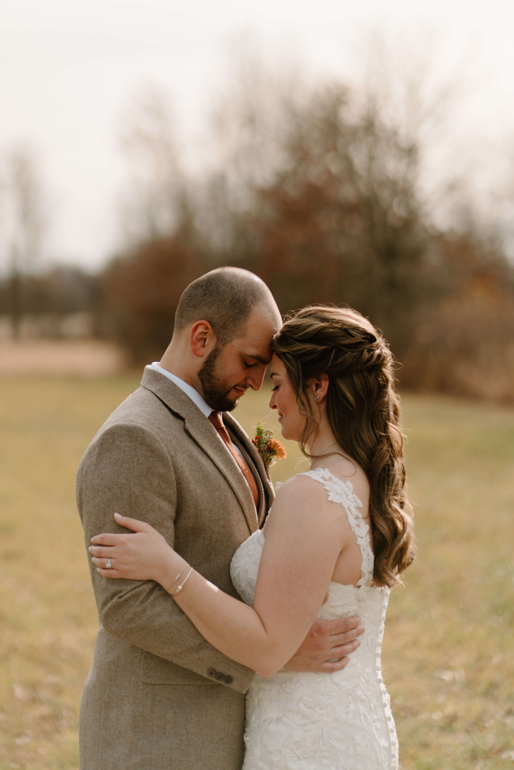 close up of bride and groom embracing, foreheads leaned together, in an open field