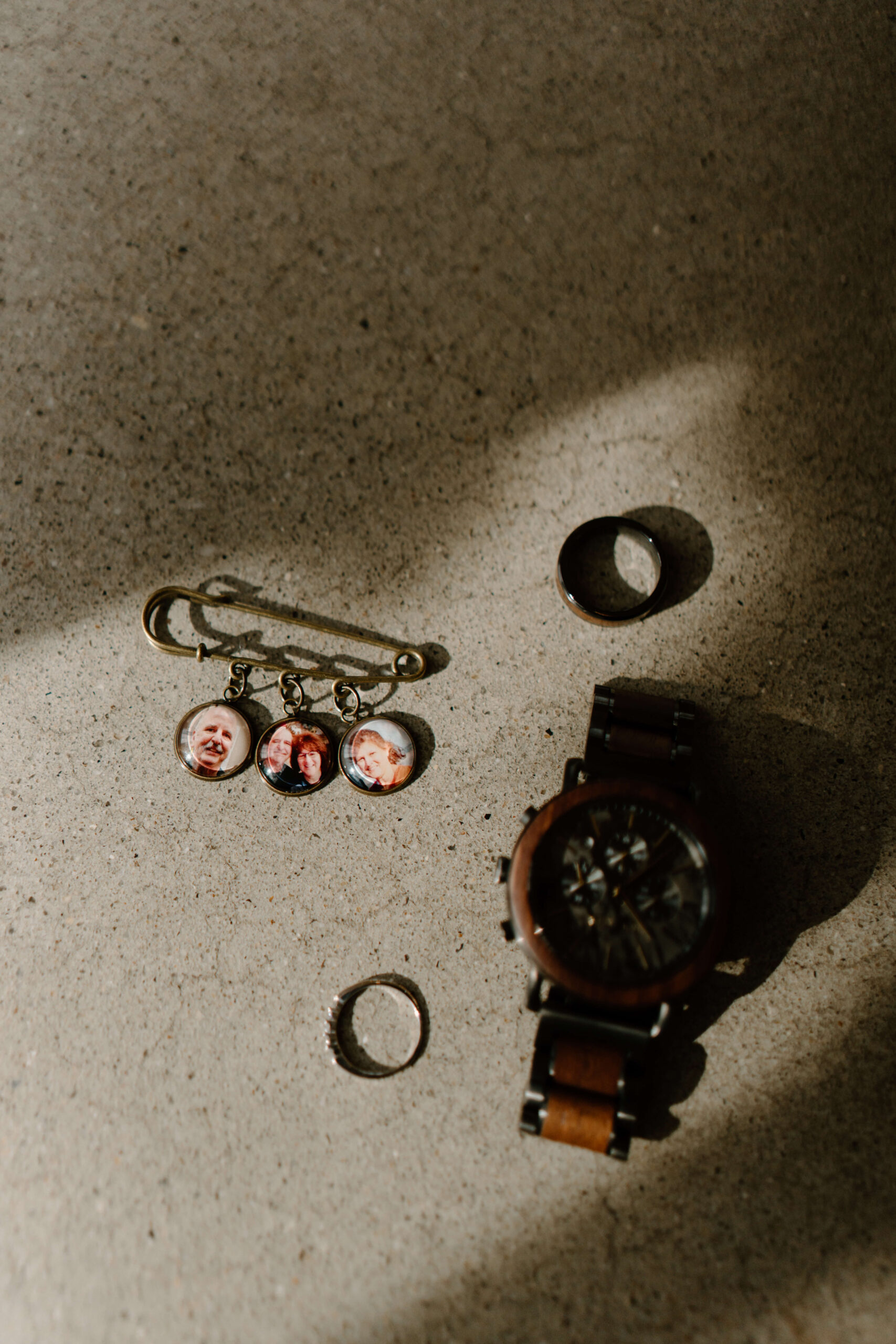 groom's watch, wedding band, and bride's wedding band, next to a memorial pin with three images of groom's parents'
