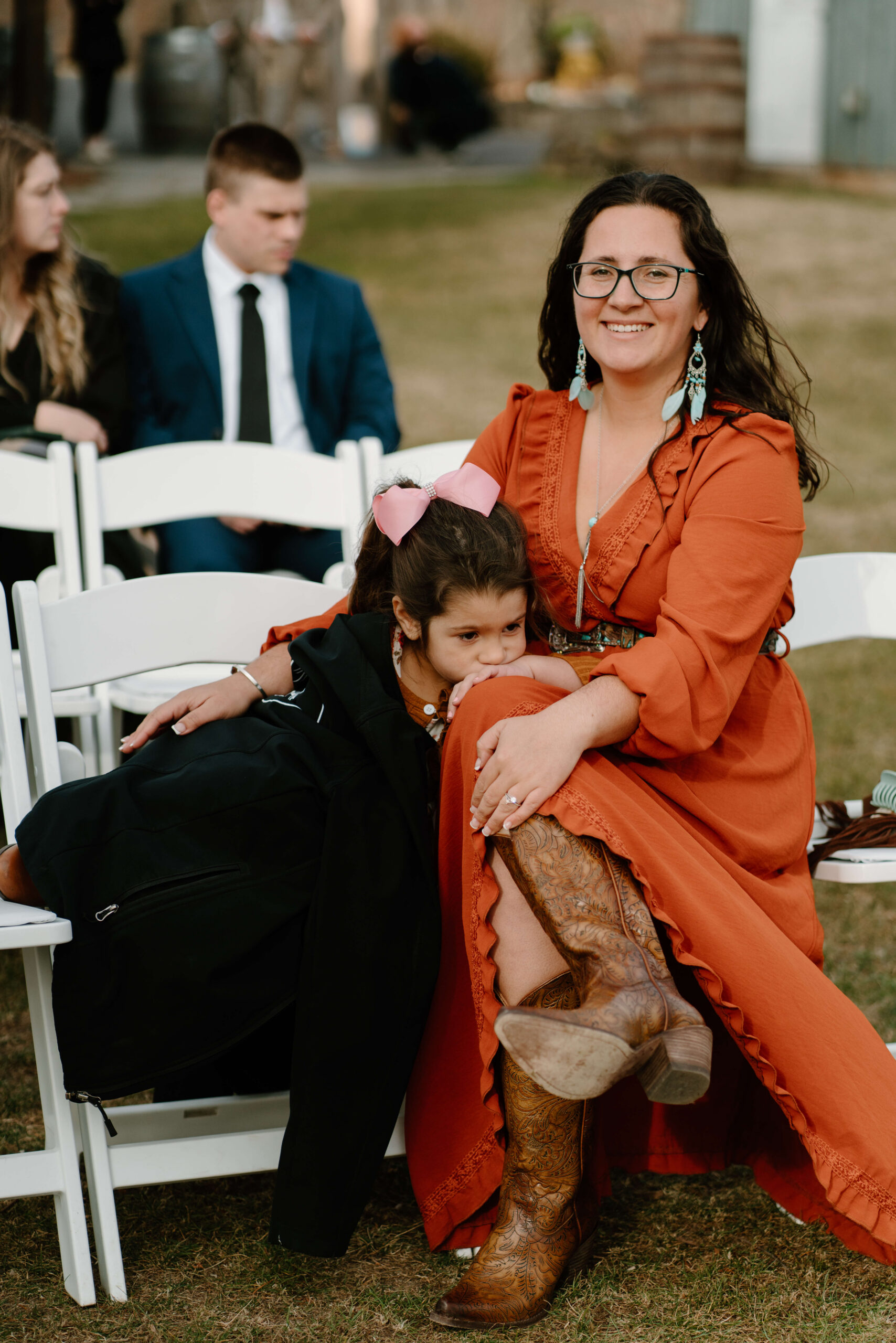 wedding guest smiling while her young daughter leans on her leg