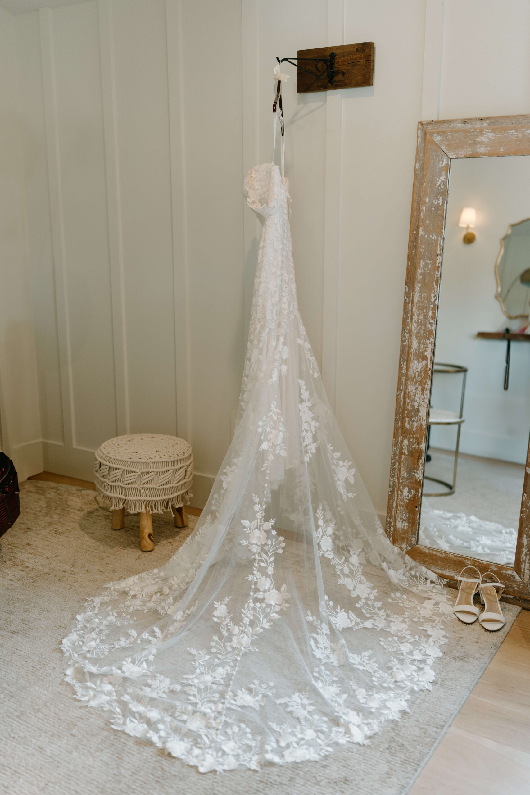 wedding dress with long lace train hanging in white bridal suite