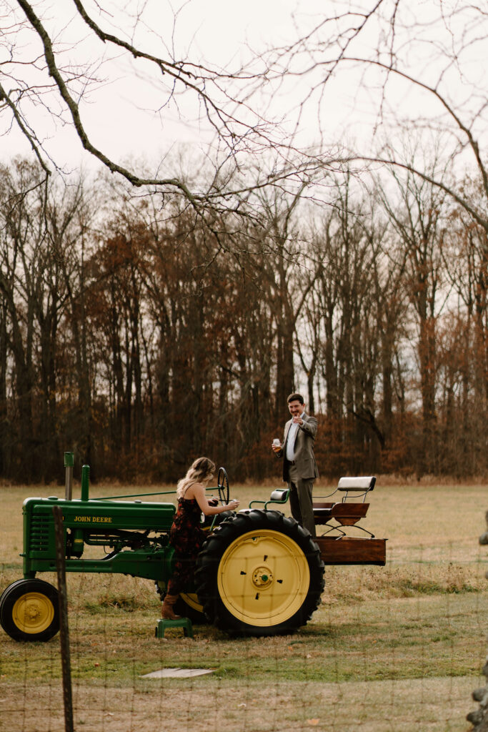 two guests climbing on an antique green John Deere tractor during cocktail hour