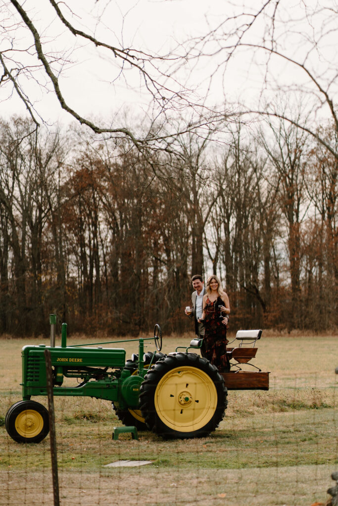 two guests climbing on an antique green John Deere tractor during cocktail hour