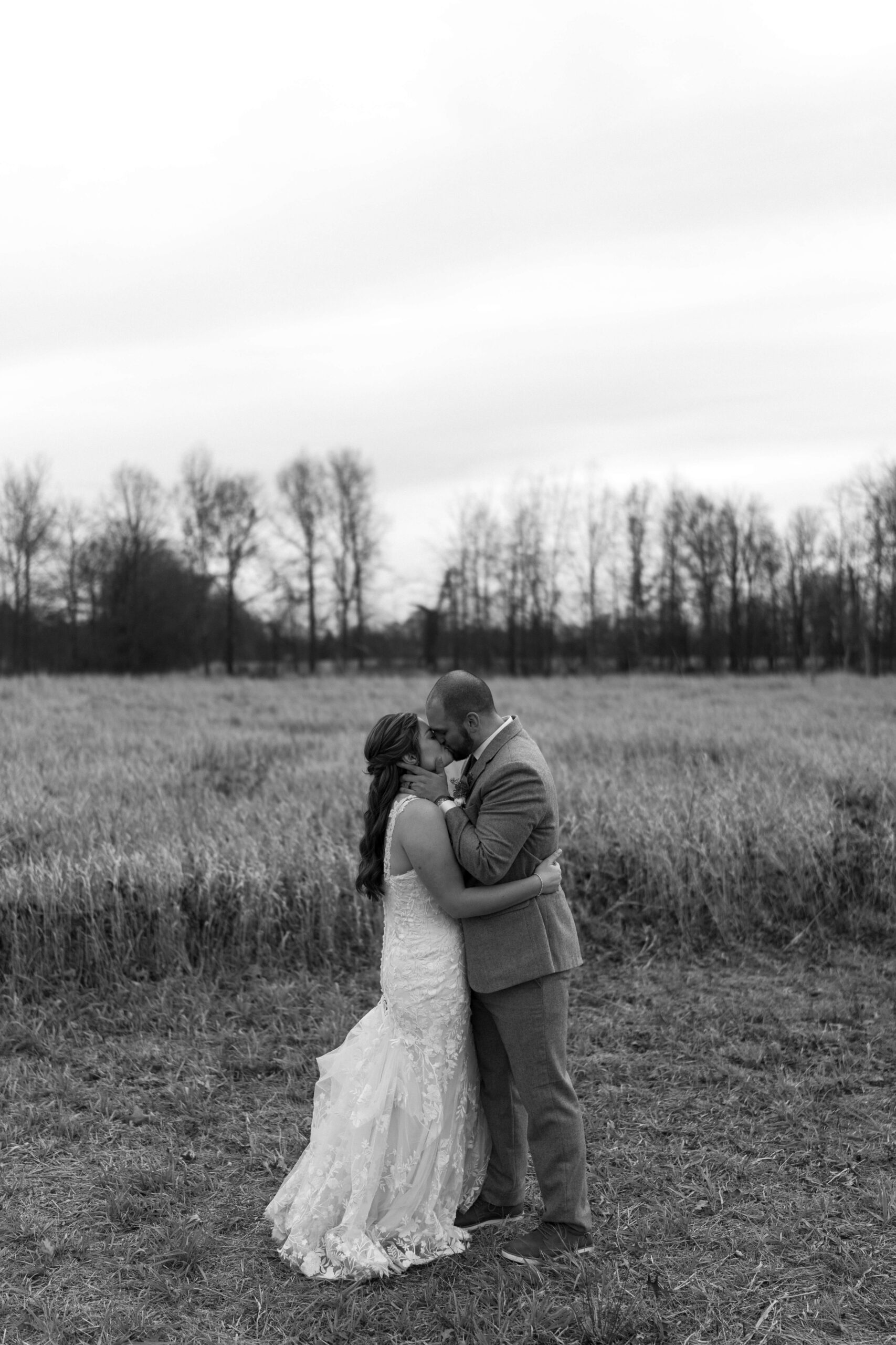 black and white image of groom holding bride's face and kissing her in a wide open field
