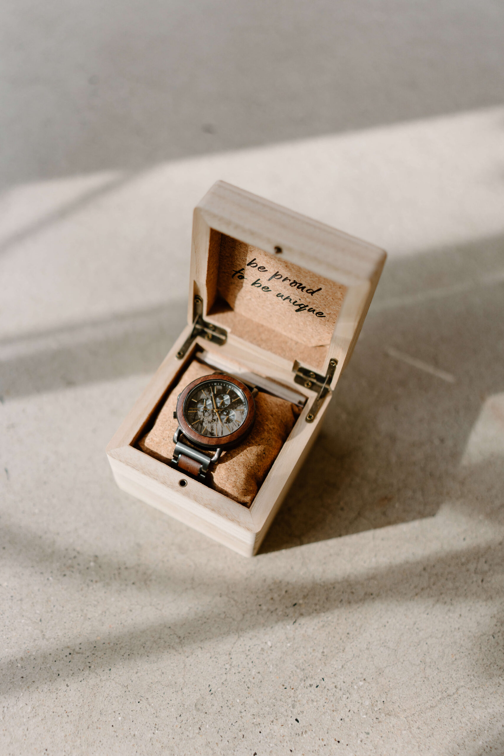 a watch in a wooden box with the words "be proud to be unique" inside the lid