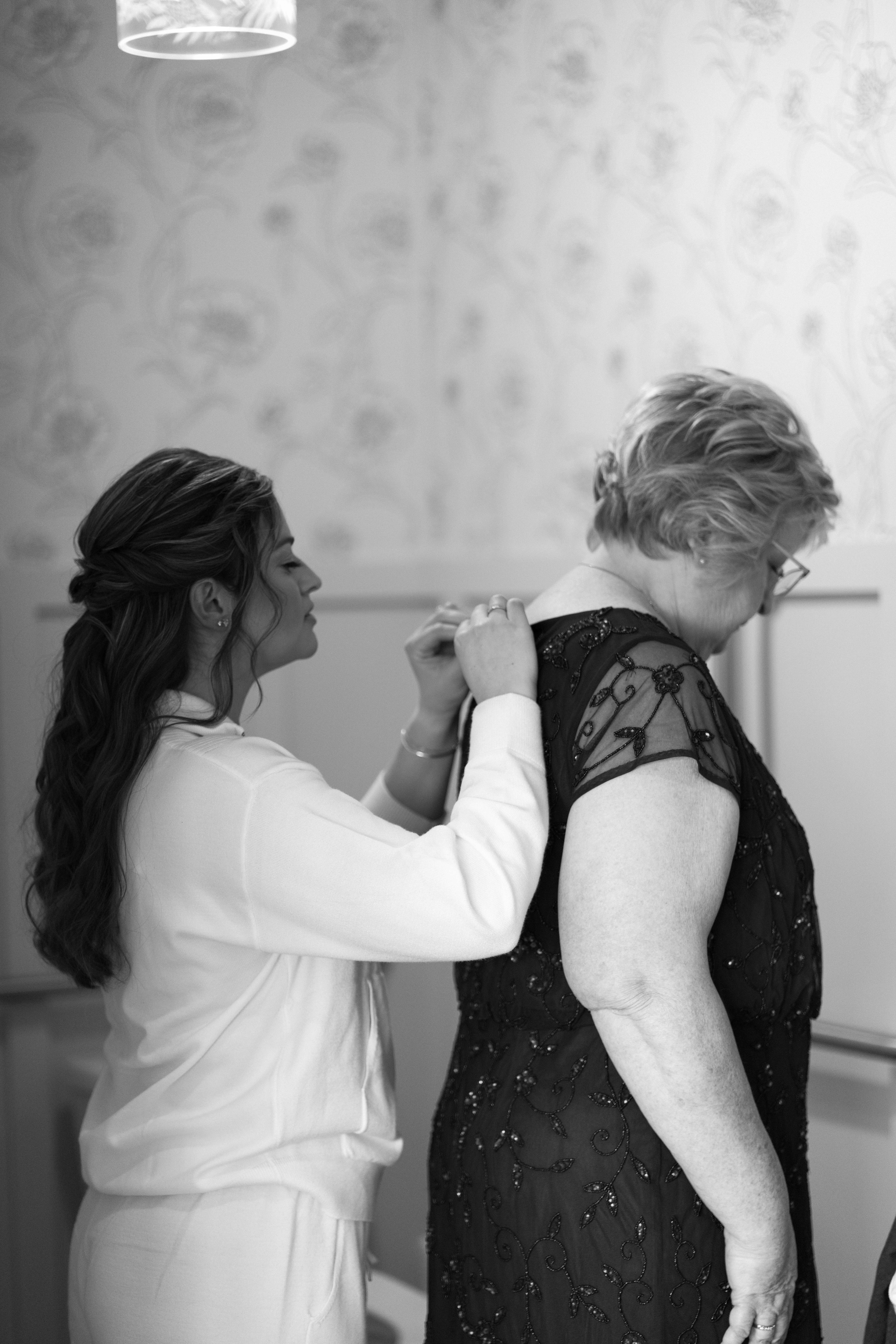 bride helping her mother into her dress before a wedding ceremony