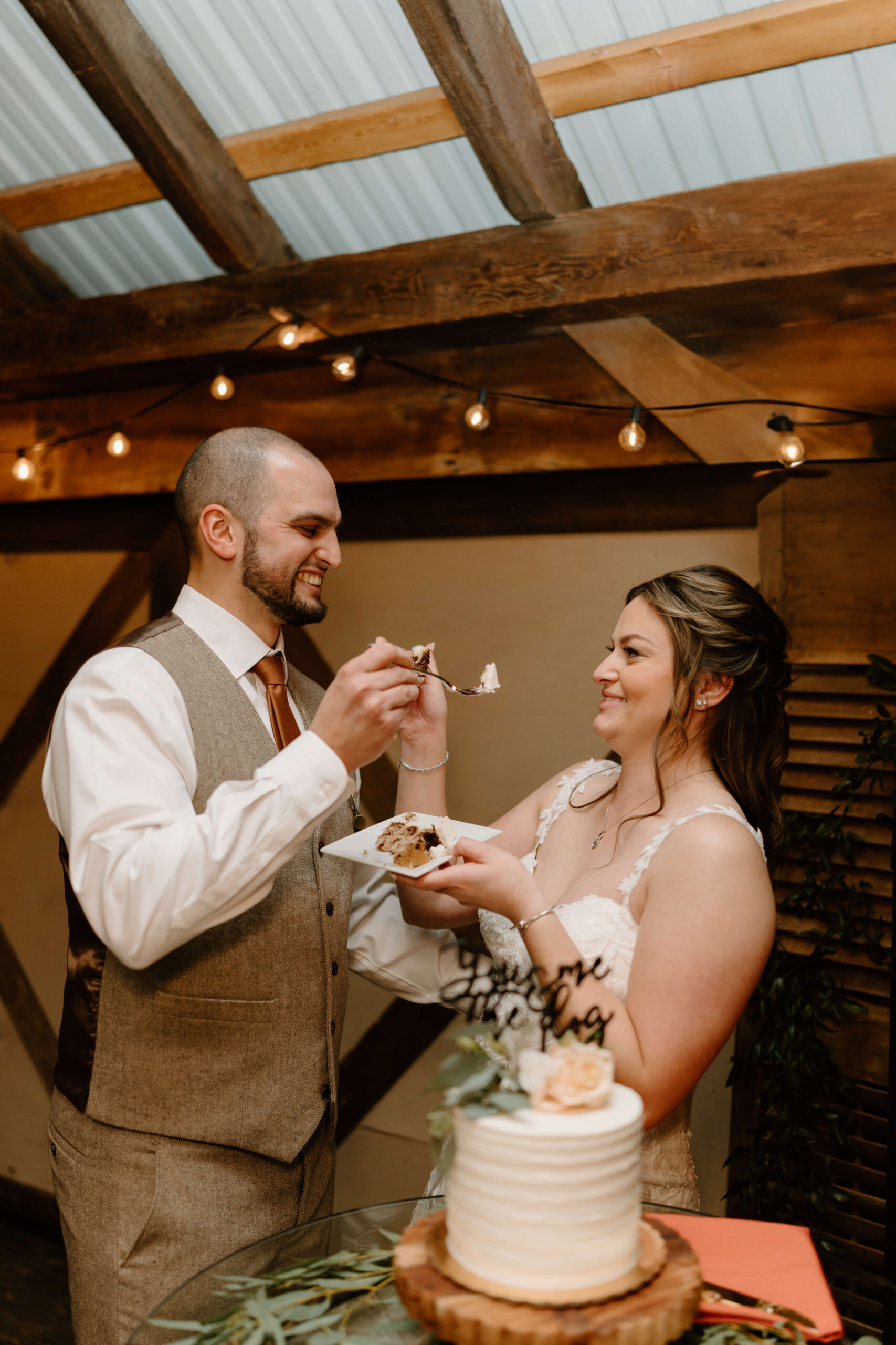 bride and groom smiling while feeding each other a slice of wedding cake
