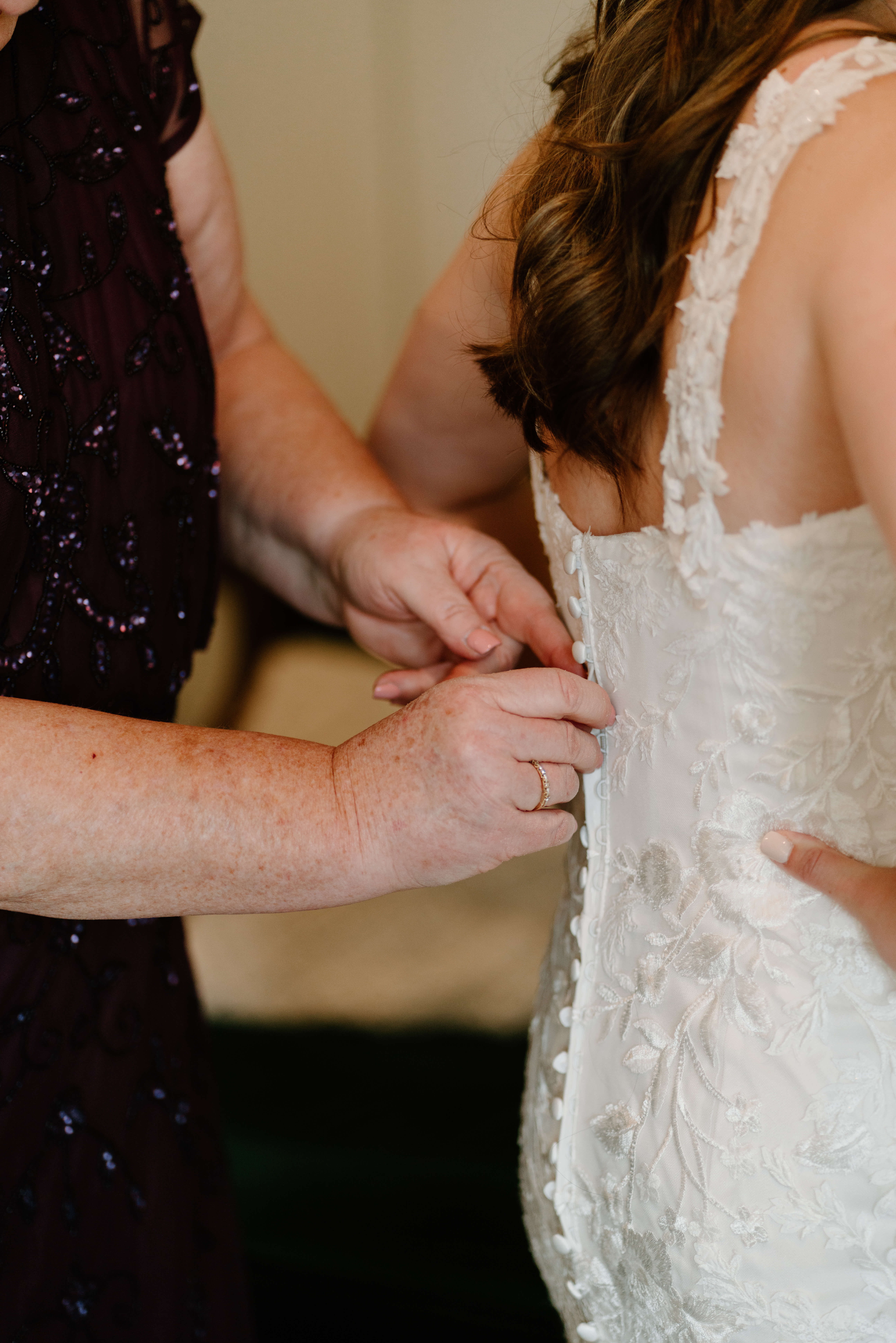 close up of mother of the bride's hands buttoning the bride's wedding dress