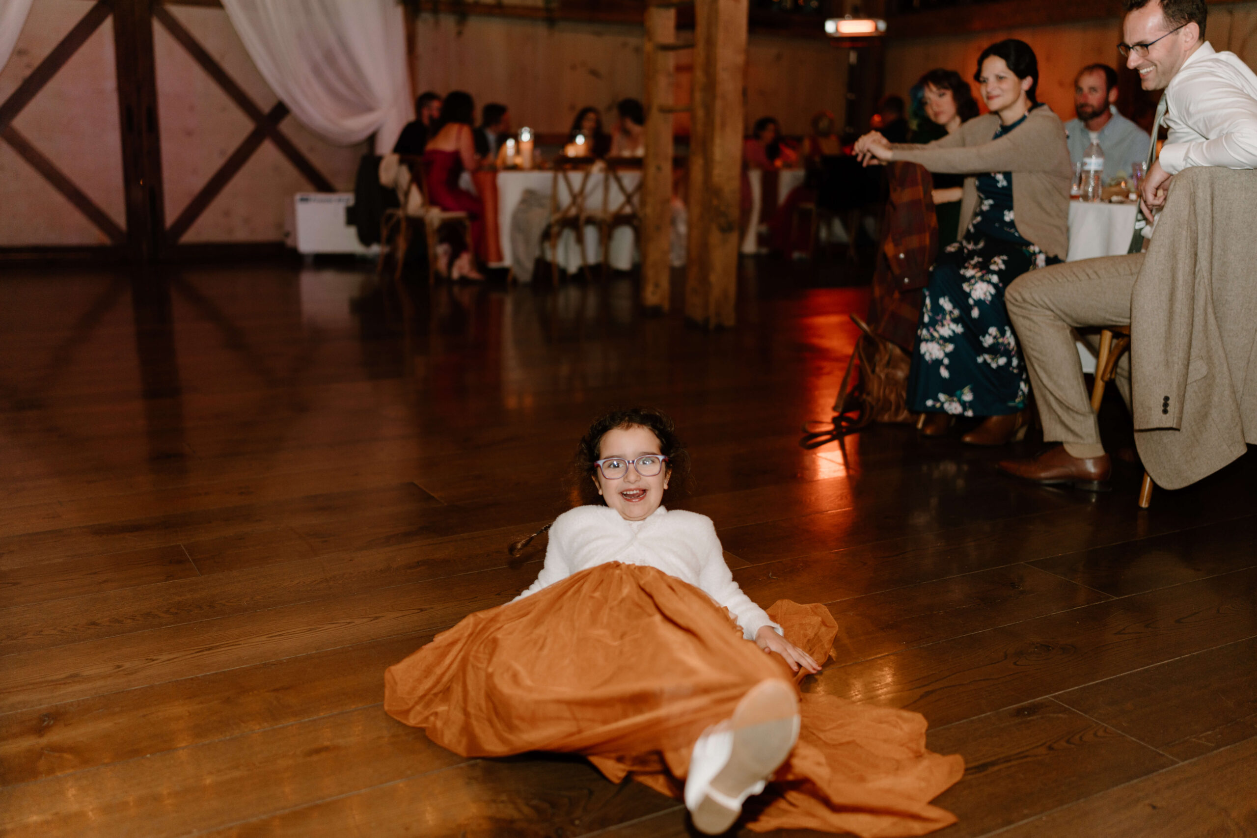 niece of the groom sliding across the dance floor on her tulle dress during wedding reception