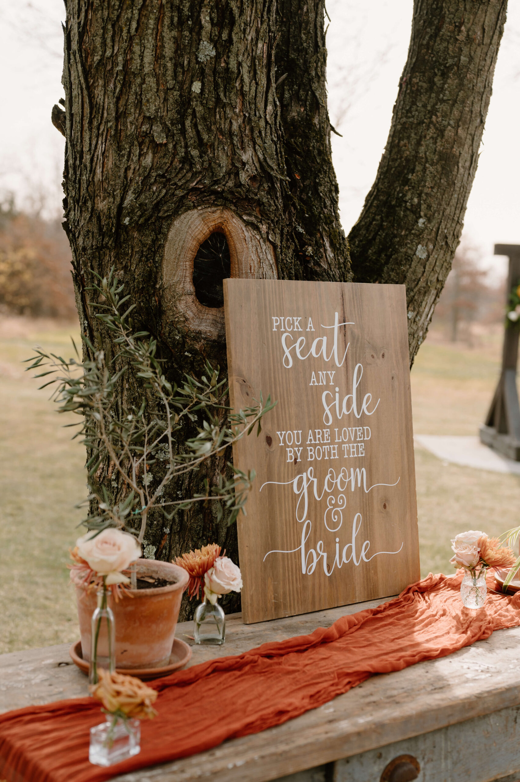 outdoor display reading "pick a seat, any side, you are loved by both the groom & bride"